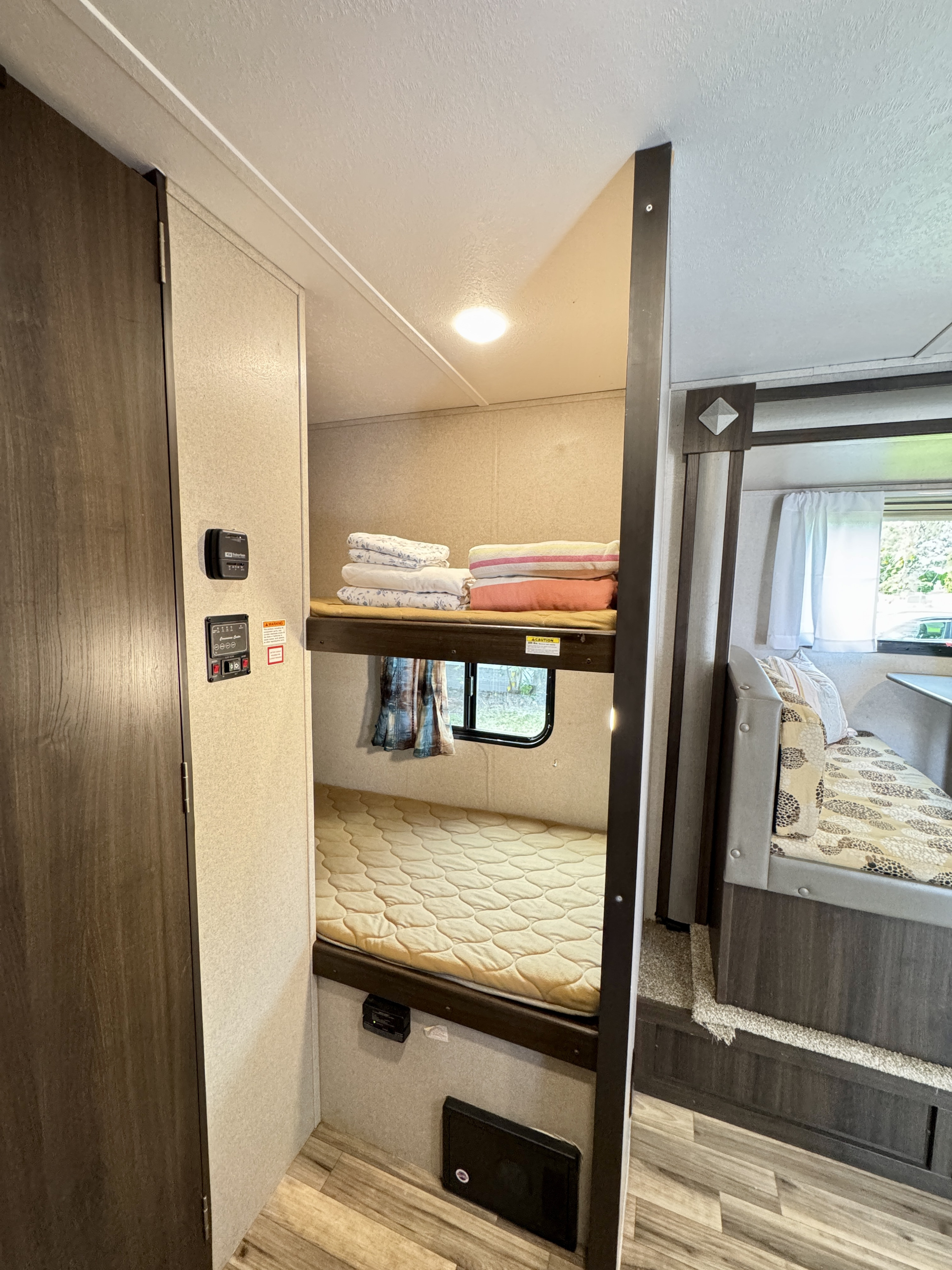 Cozy rv rental interior: view of bunk beds with bedding, a window, controls, and a portion of a dinette seat.. Keystone RV Springdale 2019
