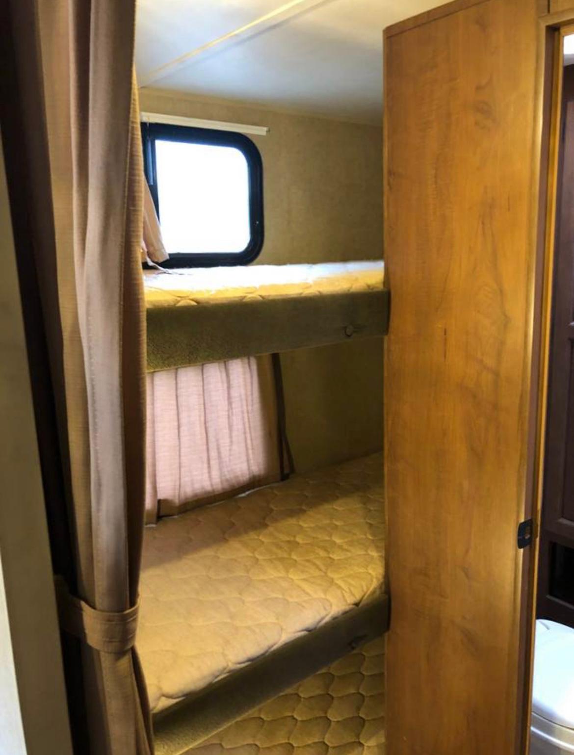 RV rental: A bright window overlooks two bunk beds with padded mattresses and soft curtains, offering comfy sleeping space.. Jayco Jay Feather Ultra Lite 2014