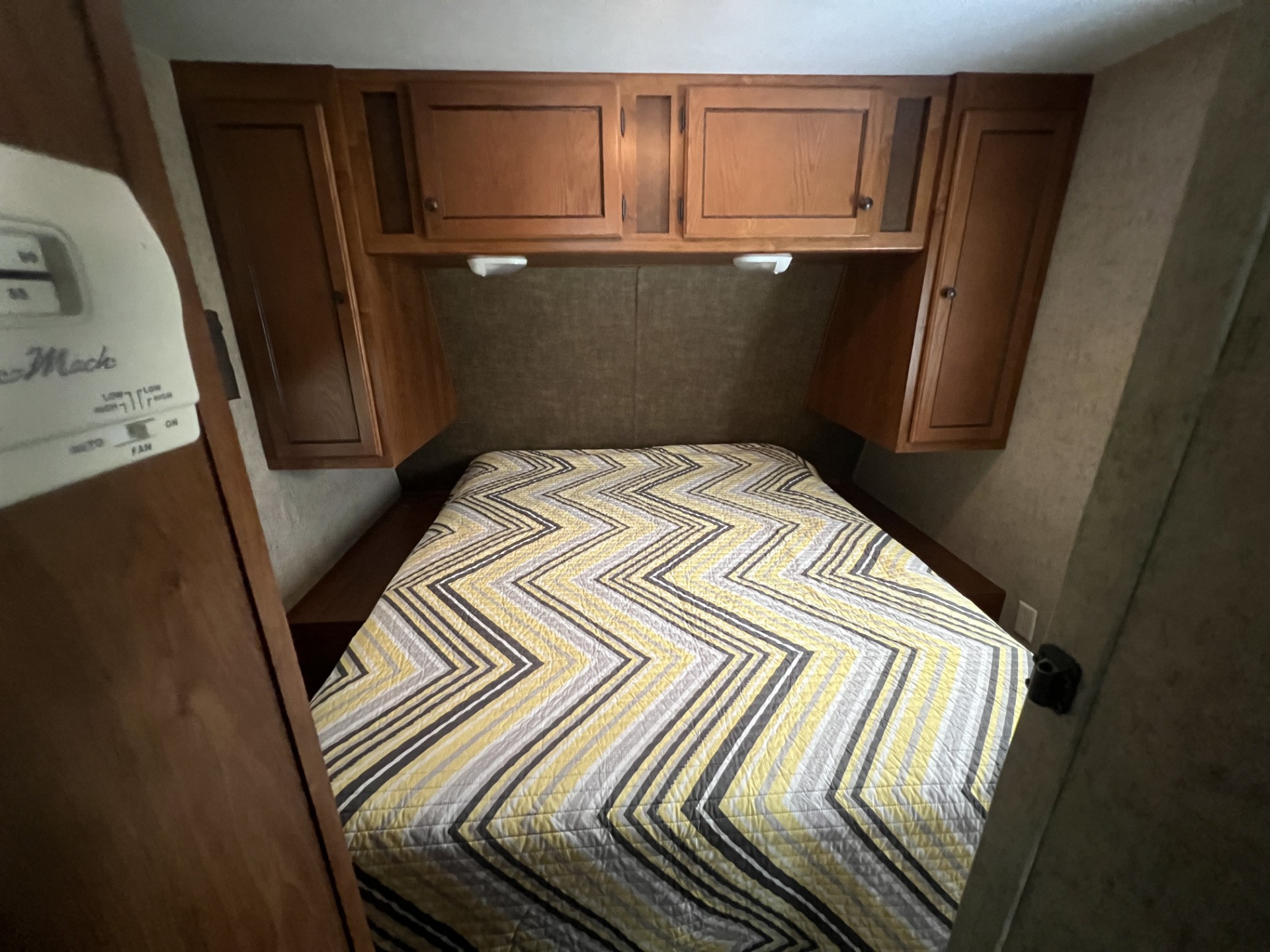 Cozy RV rental bedroom featuring a bed with a chevron comforter, wooden overhead cabinets, and built-in storage.. Heartland RVs Trail Runner 2014