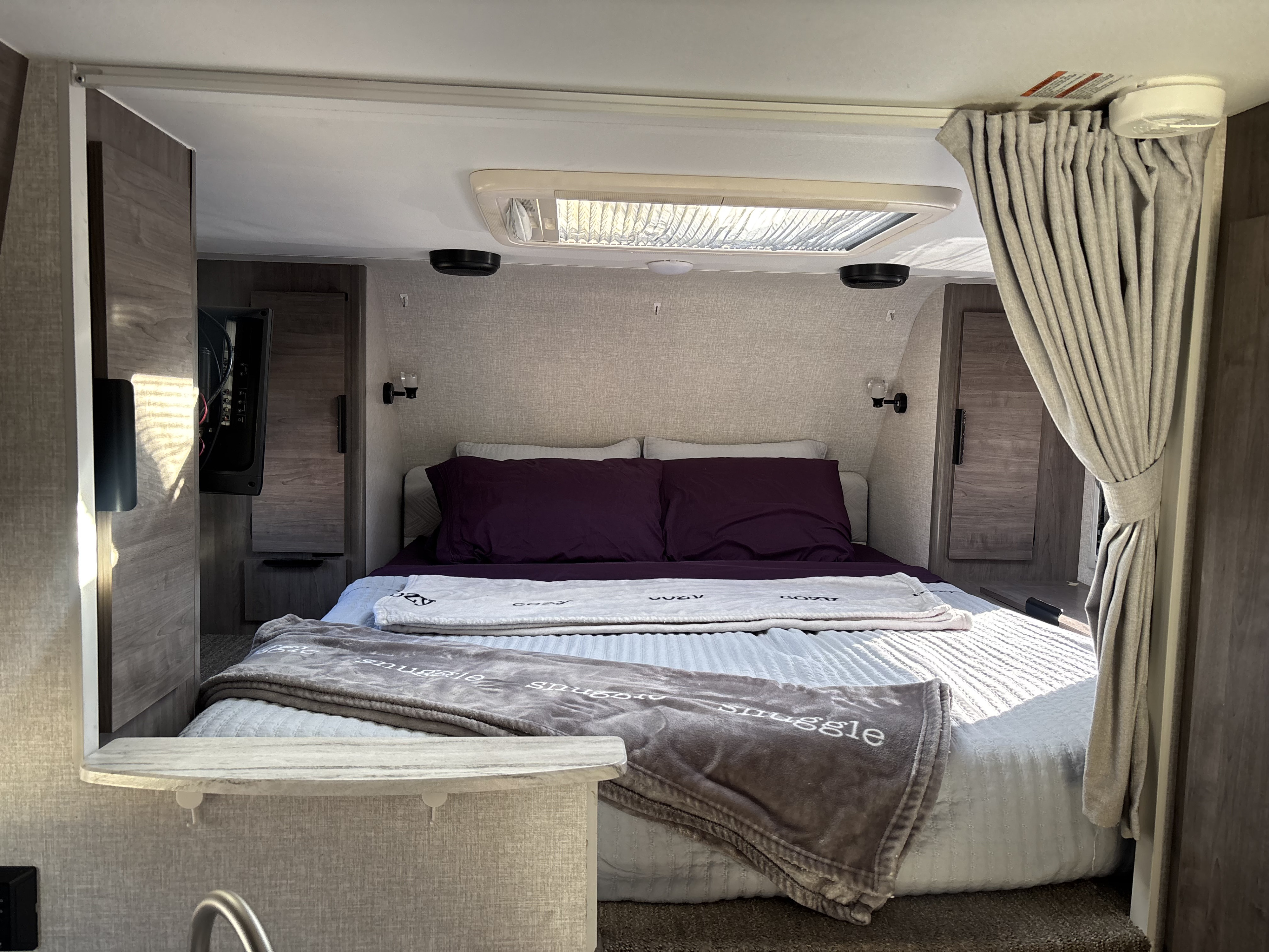 This cozy RV rental bedroom features a large bed with purple bedding, skylight, and TV, ready for a comfortable stay.. Lance 850 2022