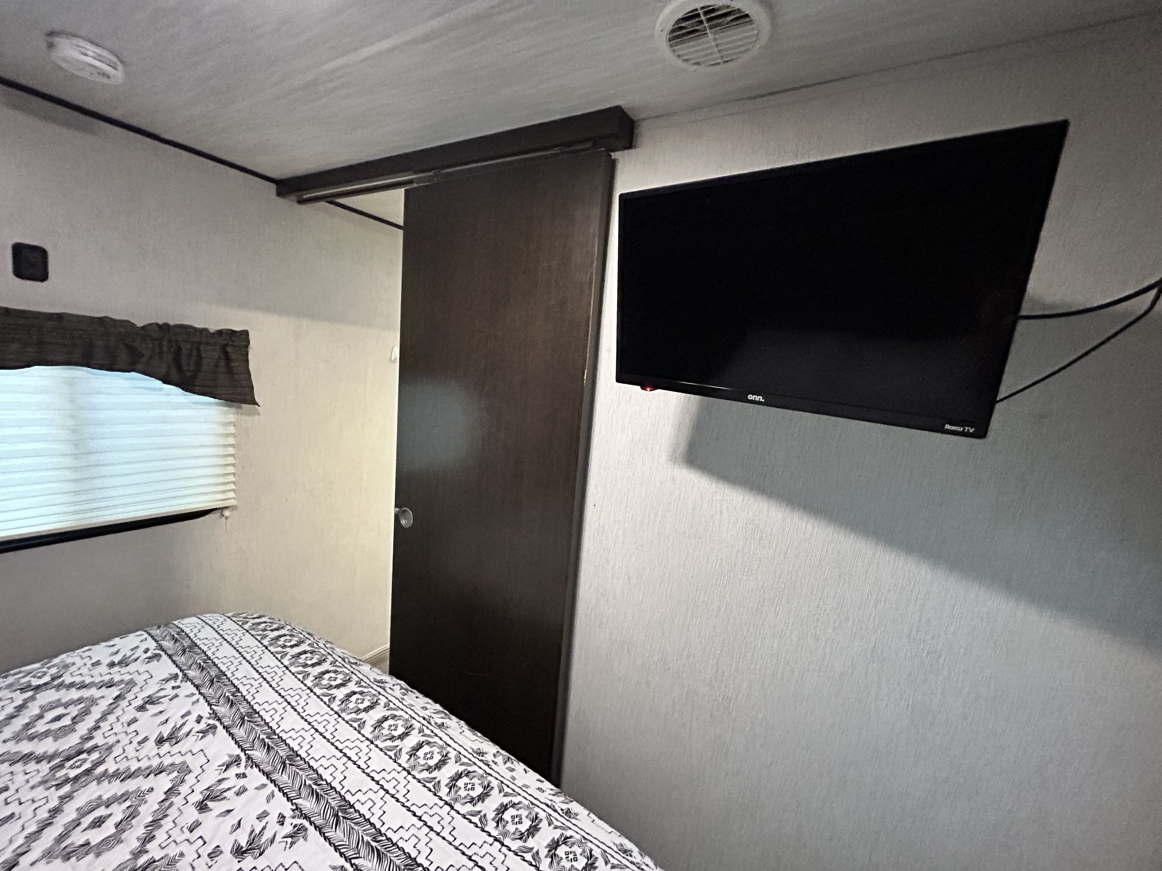 Cozy RV rental bedroom featuring a mounted TV, patterned bed, and space-saving sliding door in a compact interior.. Heartland RVs Trail Runner SLE 2019