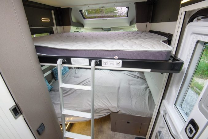 Inside an RV rental: a cozy bunk bed setup featuring a top mattress, a lower bed with sheets, and an access ladder. Ideal for family adventures.. chausson Exclusif line 2024