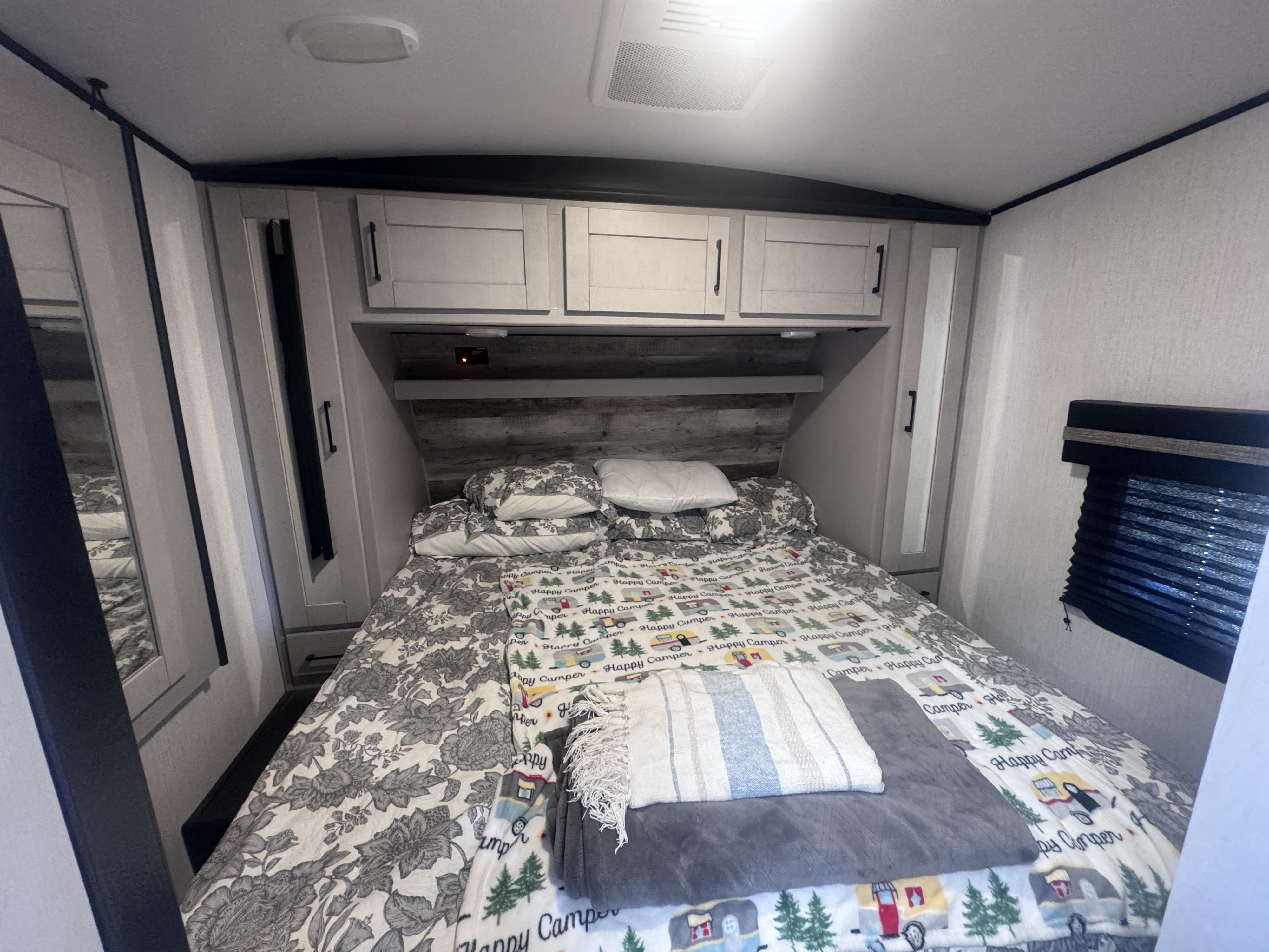 Cozy RV rental bedroom with a comfy bed, overhead cabinets, and window blinds. Perfect for camping trips!. Heartland Torque 2022