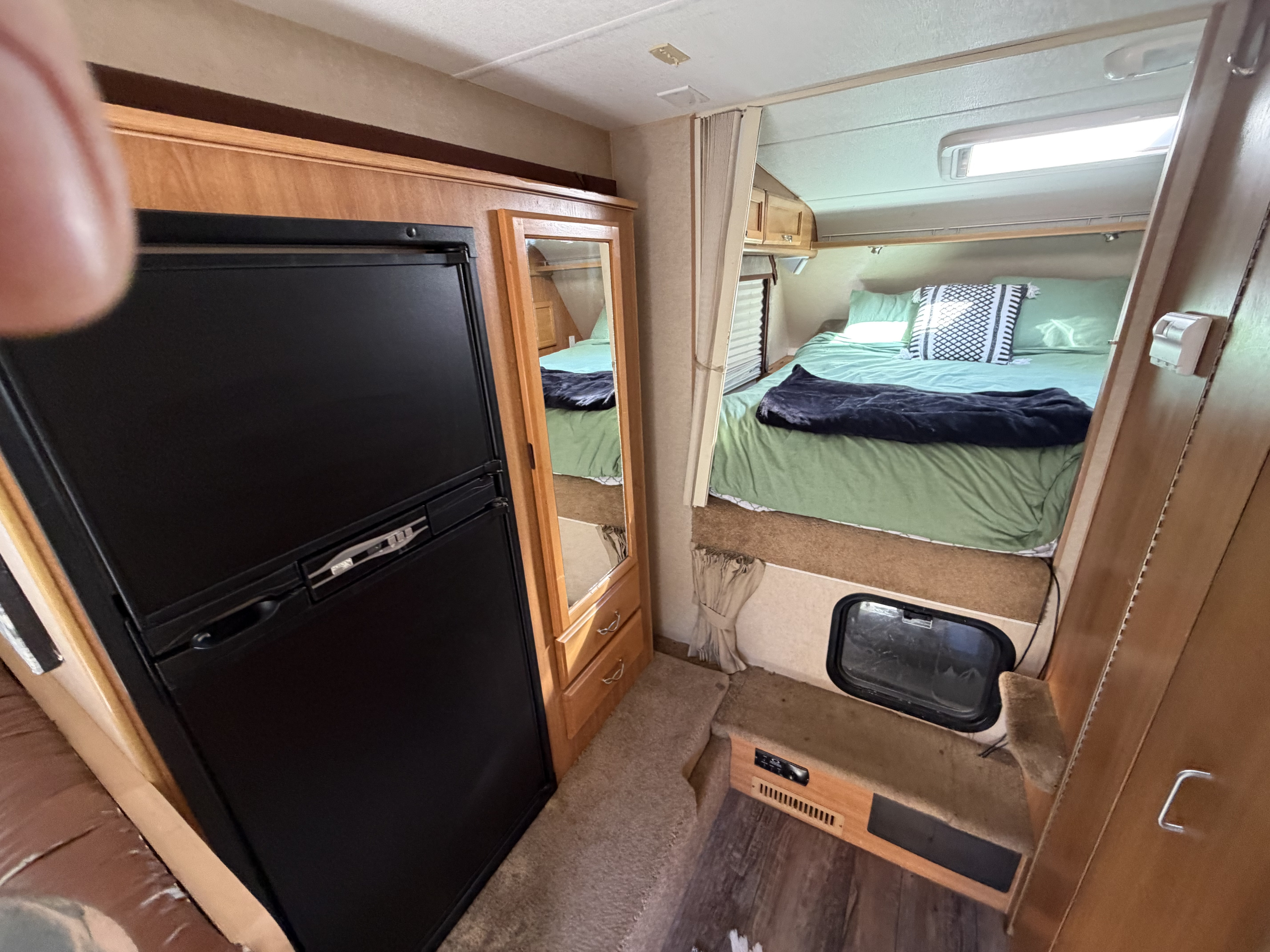 Cozy rv rental interior: A compact camper with a comfortable bed, black refrigerator, mirrored storage, and wood accents.. Ford F350 Diesel Double Cab 2017