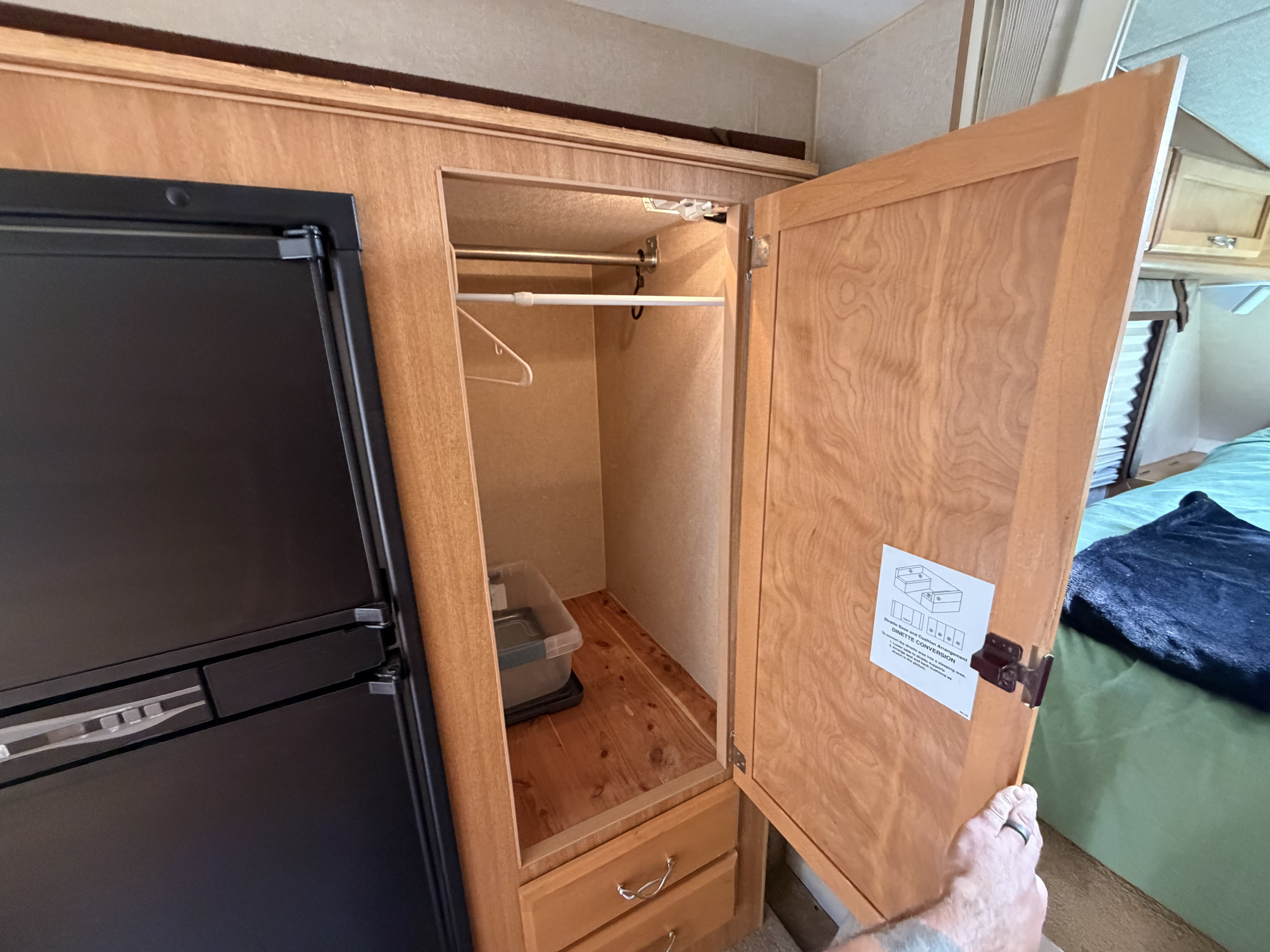 RV rental closet beside fridge, featuring a hanging rod, bin & drawers. Dinette conversion guide on door, with bed nearby.. Ford F350 Diesel Double Cab 2017