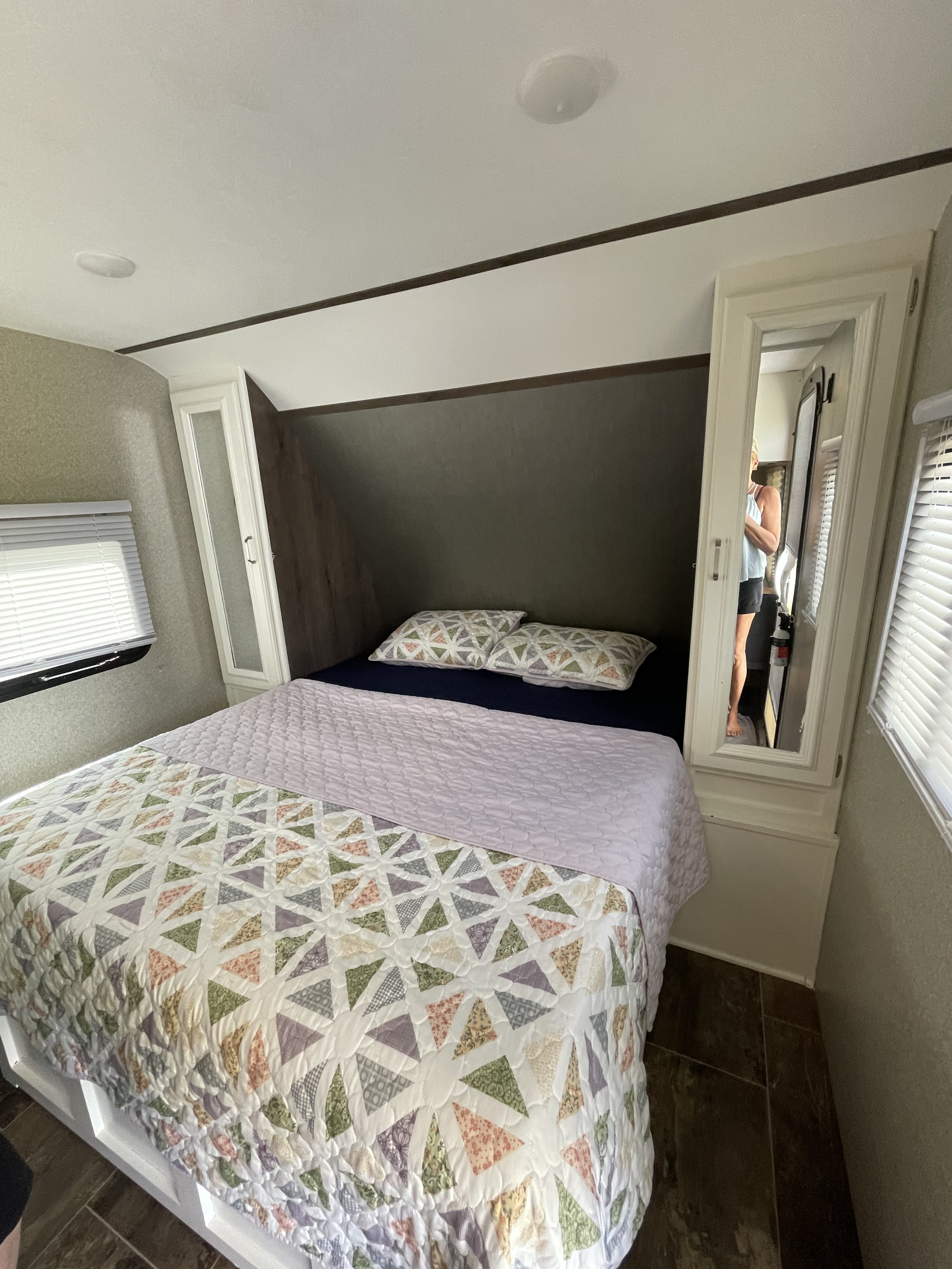 Cozy RV rental bedroom with a comfy bed, colorful quilted bedding, overhead cabinets, and a mirrored closet.. Keystone RV Passport Ultra Lite 2019