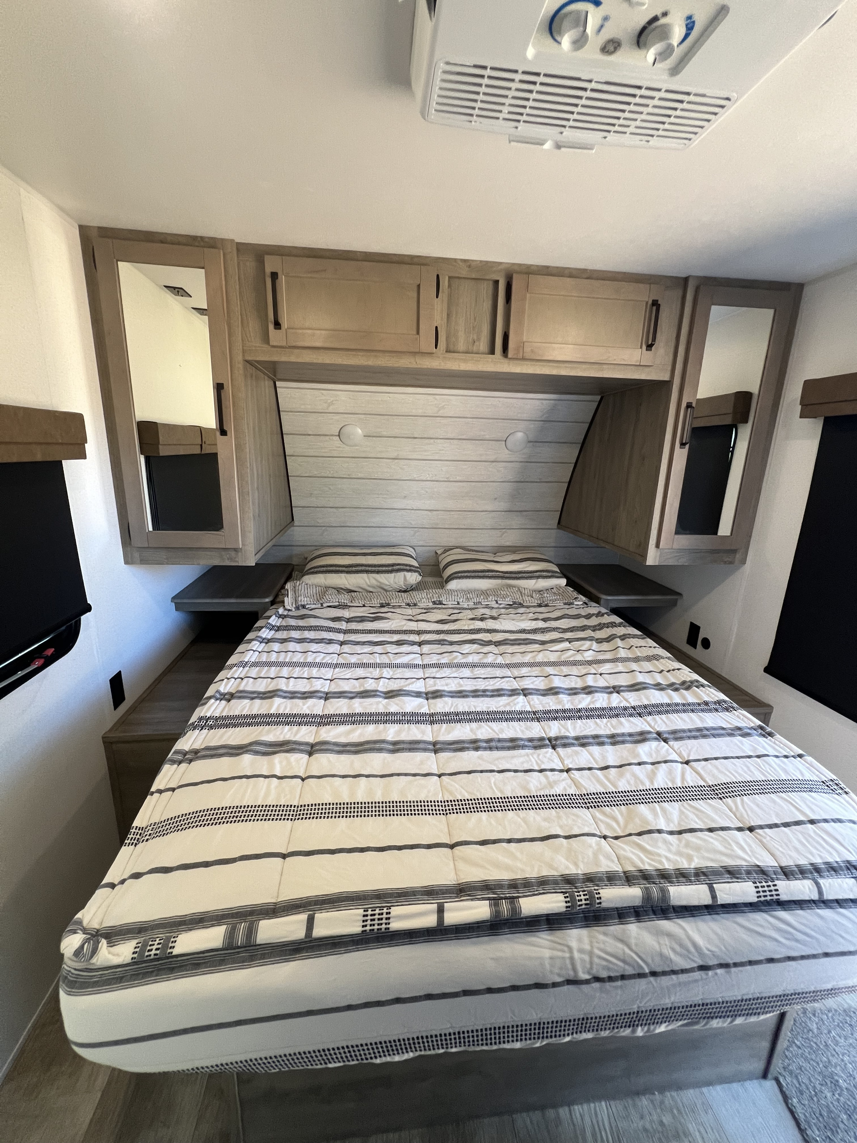 Cozy RV rental bedroom featuring a striped bed, overhead cabinets, bedside shelves, and an AC unit for comfortable travel.. Forest River Palomino Puma 2025