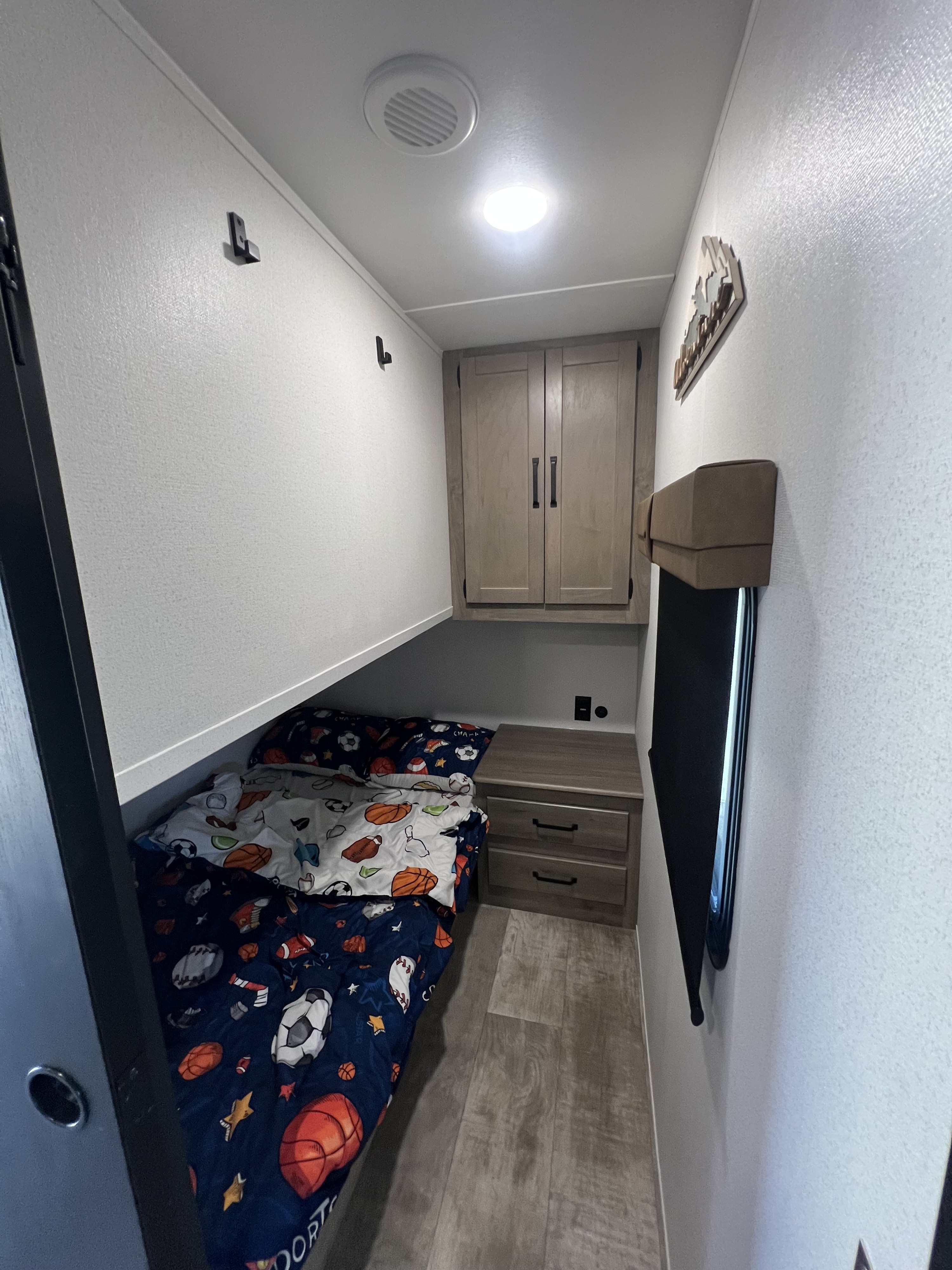 Compact RV rental bunk bedroom with sports-themed bedding, storage, outlets, and a window for comfortable stays.. Forest River Palomino Puma 2025