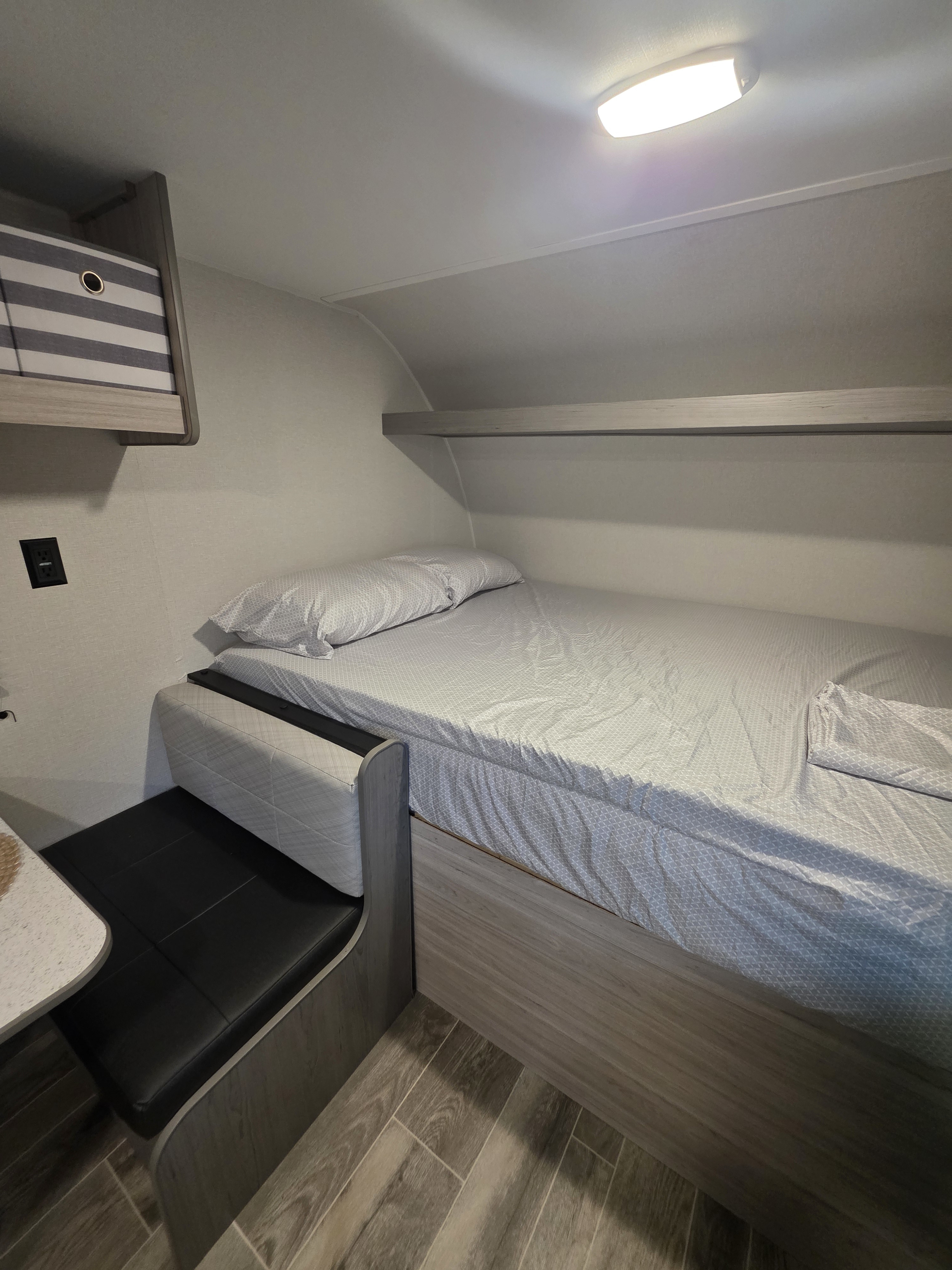 RV rental: a compact bedroom with a bed, light patterned sheets, black dinette seating, and overhead storage.. Heartland RVs Pioneer 2025