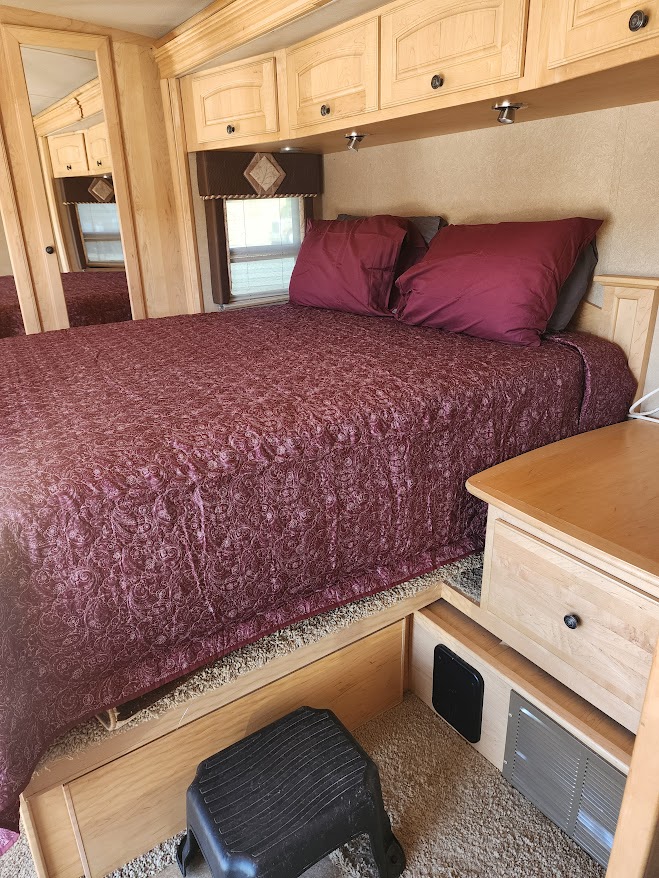 RV rental bedroom with a large bed, maroon quilt, wooden cabinetry, mirrored closet, and step stool.. Winnebago Vectra 2008