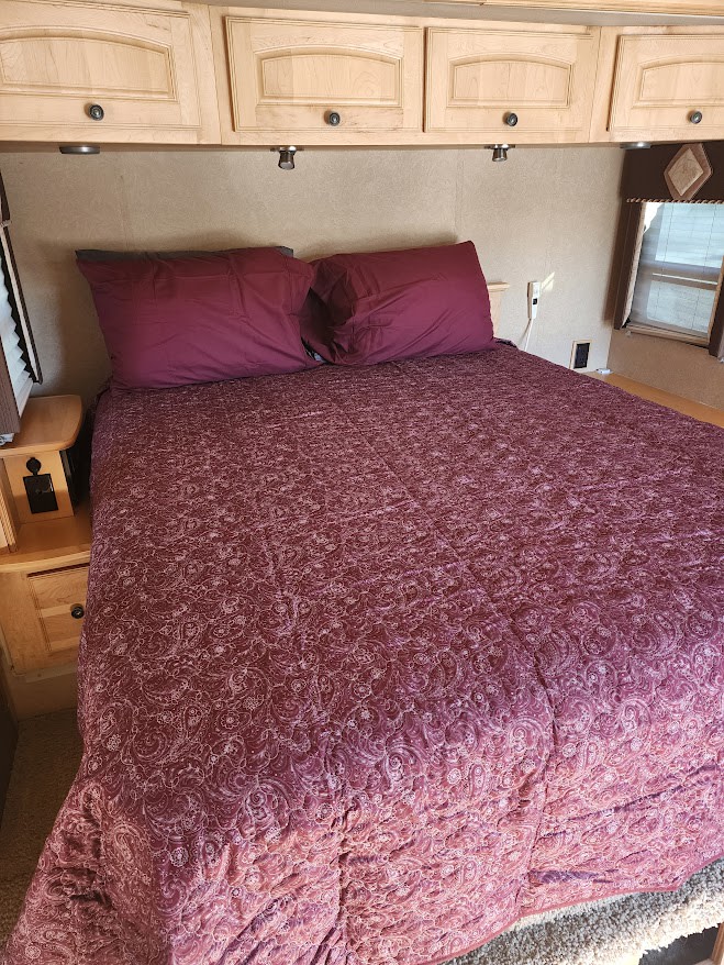 Comfortable RV rental bedroom. A large bed with maroon paisley comforter, two pillows, and wood cabinets overhead.. Winnebago Vectra 2008