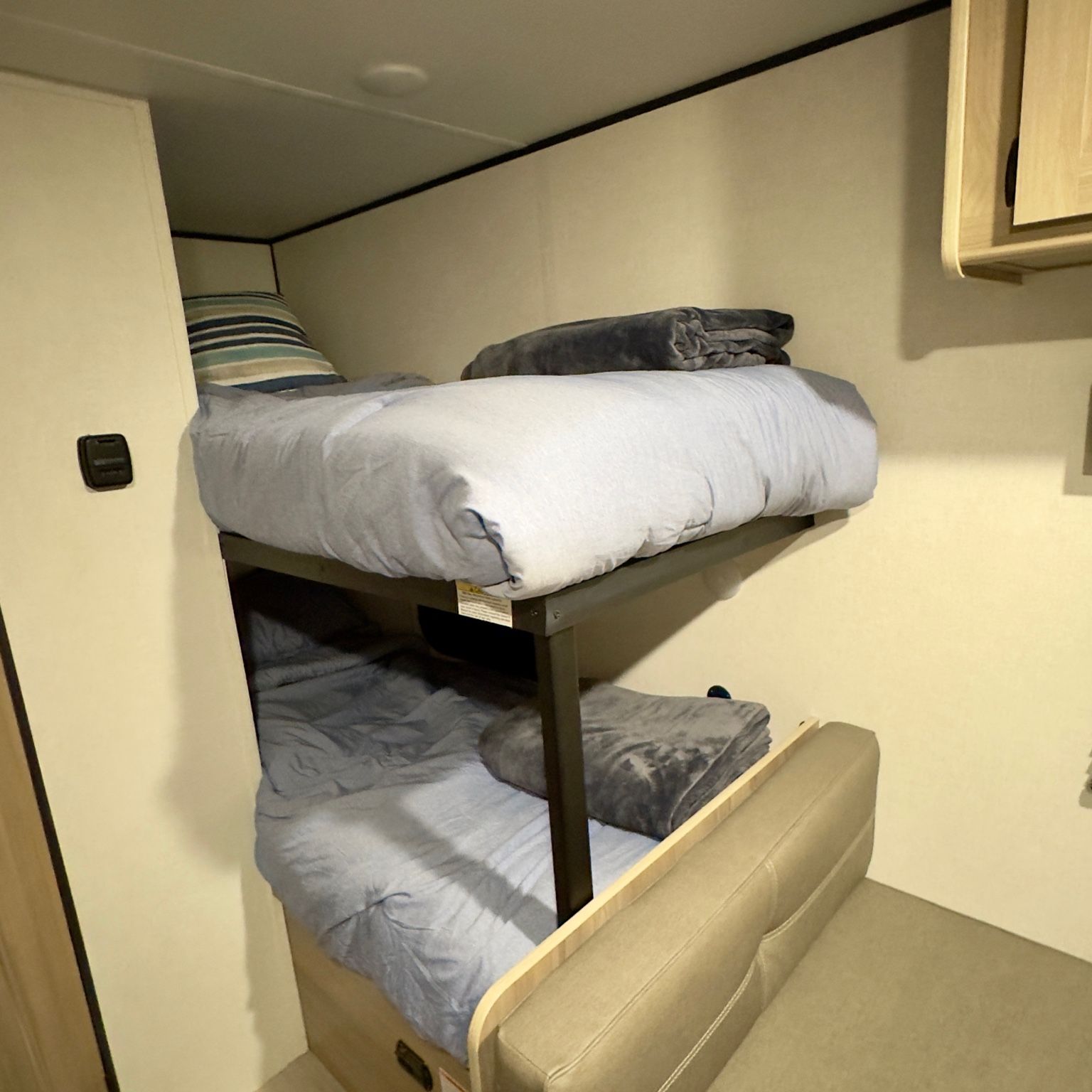 Two bunk beds with light blue bedding and grey blankets in an RV rental, alongside a cushioned bench.. Keystone RV Coleman 2025