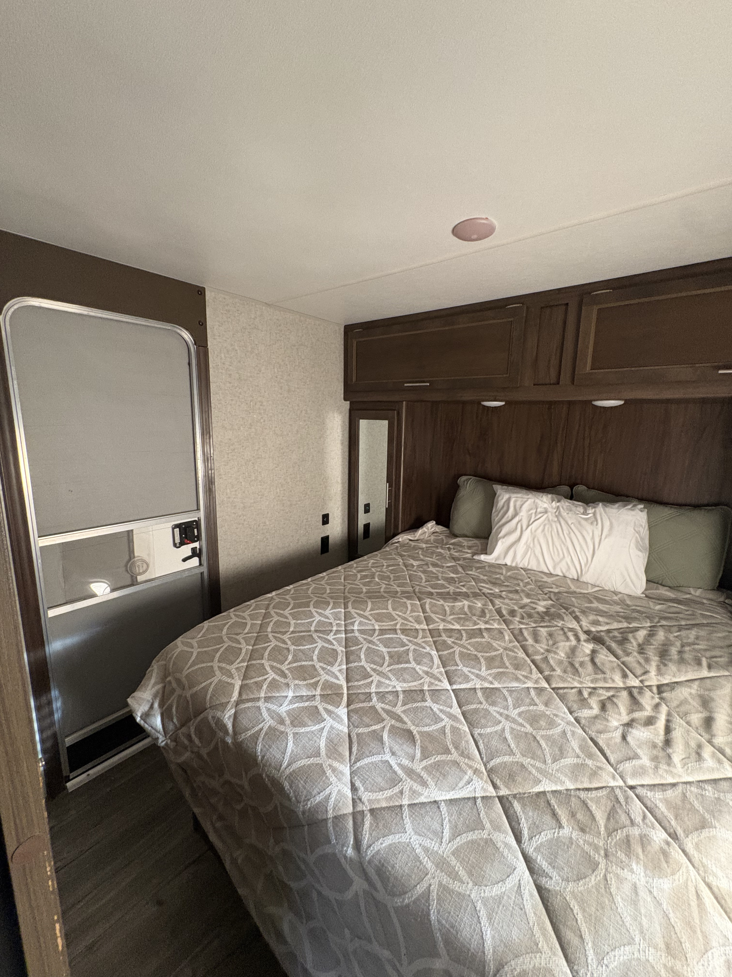 Cozy bedroom in an RV rental with a large bed, overhead cabinets, and an entry door, providing comfortable accommodations.. Forest River Cherokee 2017