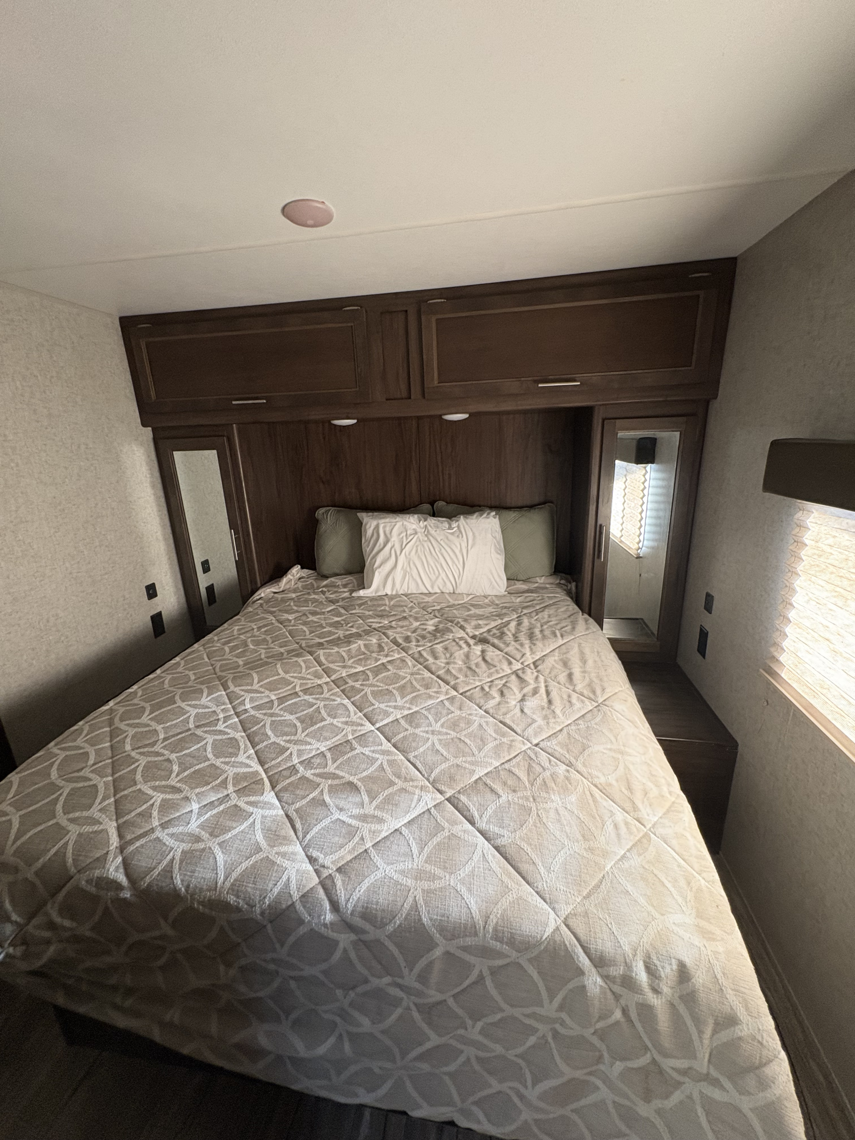 Cozy rv rental bedroom featuring a patterned bedspread, overhead cabinets, and mirrored wardrobes for compact living.. Forest River Cherokee 2017