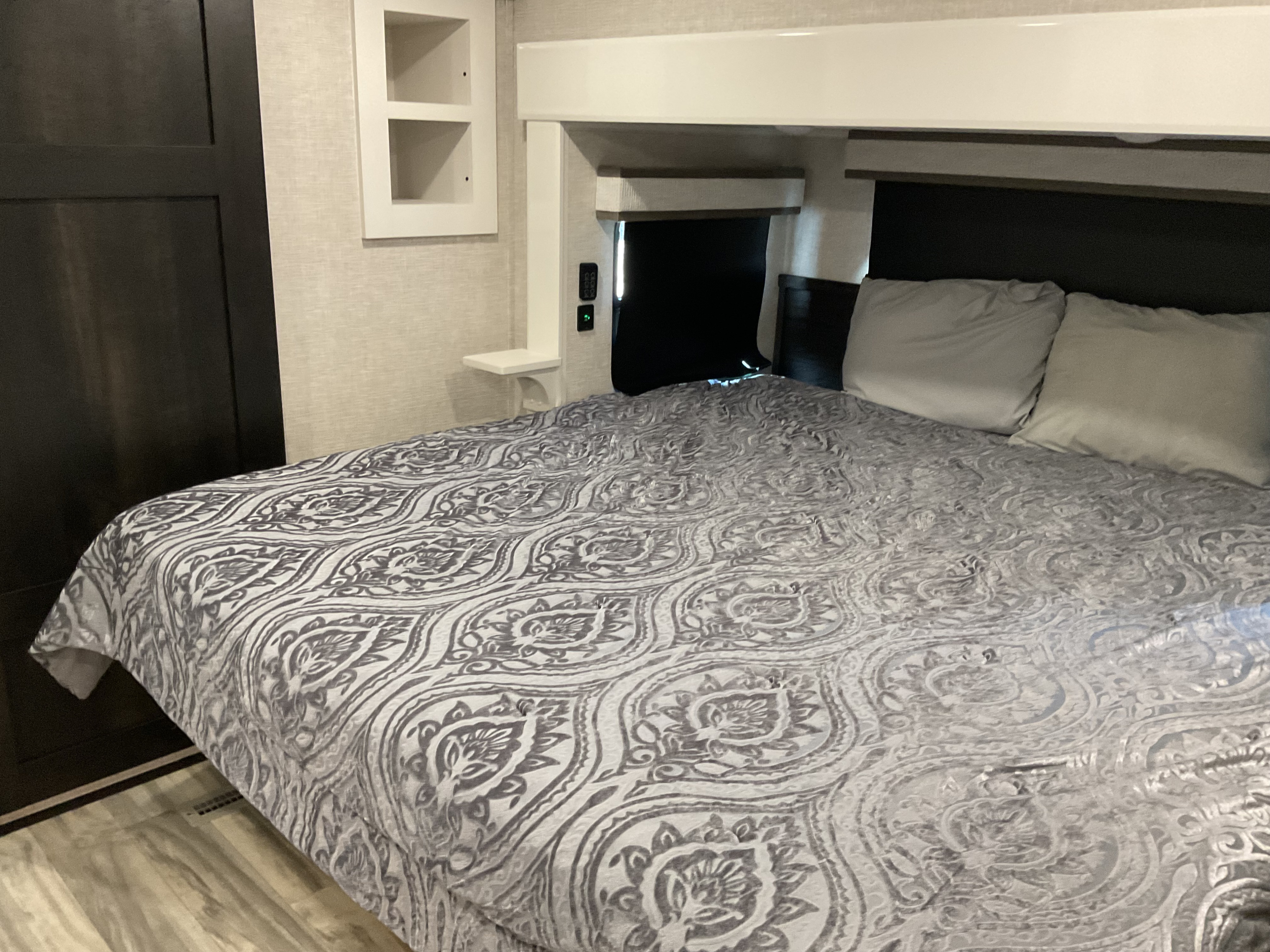 Comfortable rv rental bedroom with a grey patterned bedspread, pillows, built-in shelving, and useful charging ports.. Jayco Pinnacle 2025