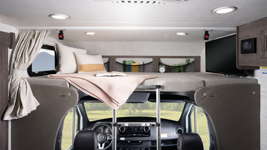 This RV rental interior features a comfortable cab-over bunk bed, complete with a TV and storage, overlooking the vehicle's driver cabin.. Entegra Coach Qwest SE 2025