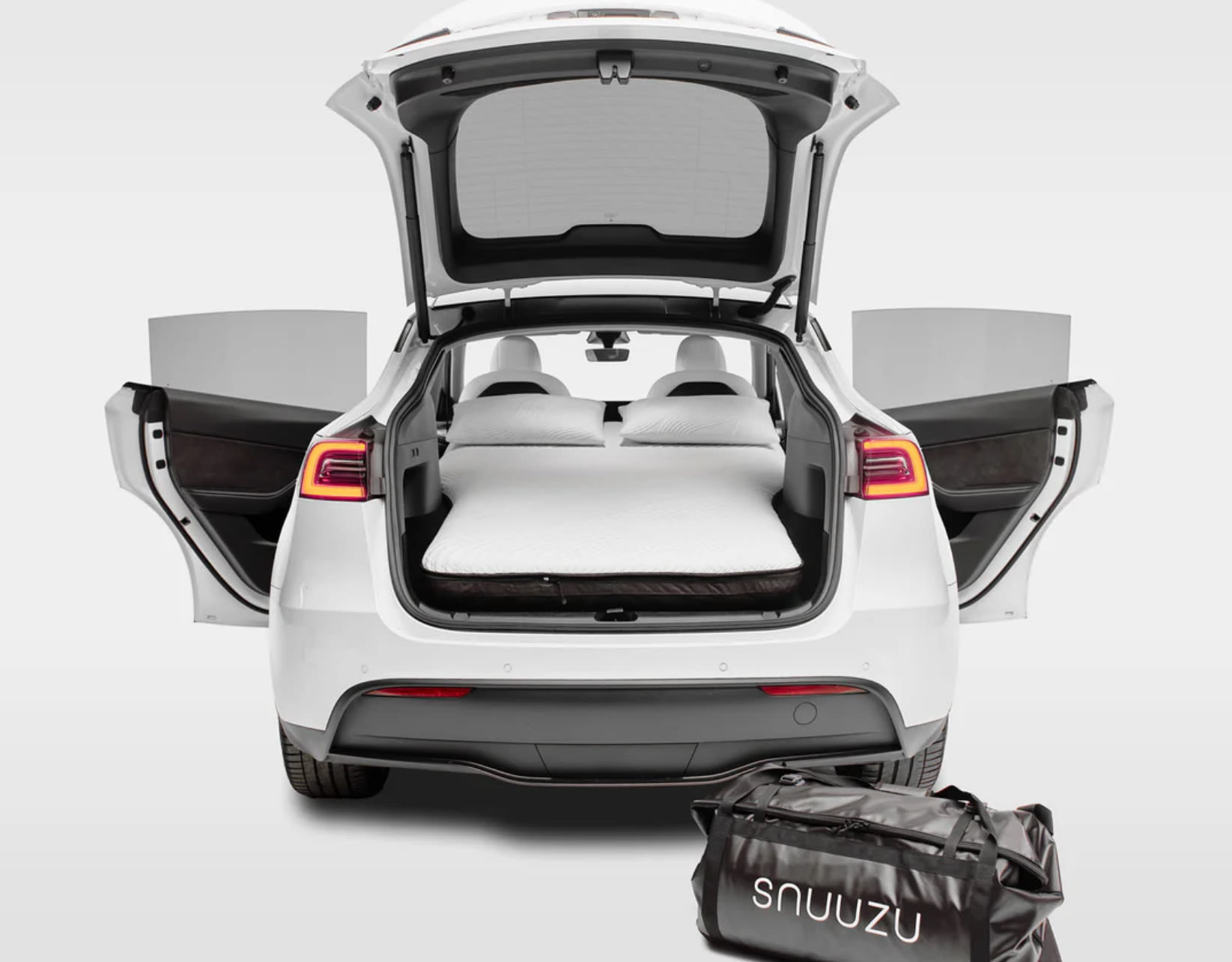 White Tesla Model Y with open trunk/doors, a mattress, and pillows inside, ideal for car camping. A smart RV rental alternative.. Tesla Model Y 2022