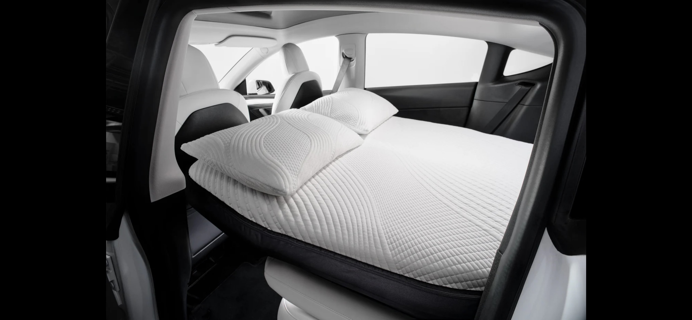 Inside a car, a comfortable white mattress and pillows create a sleeping setup, offering an RV rental feel for road trips.. Tesla Model Y 2022