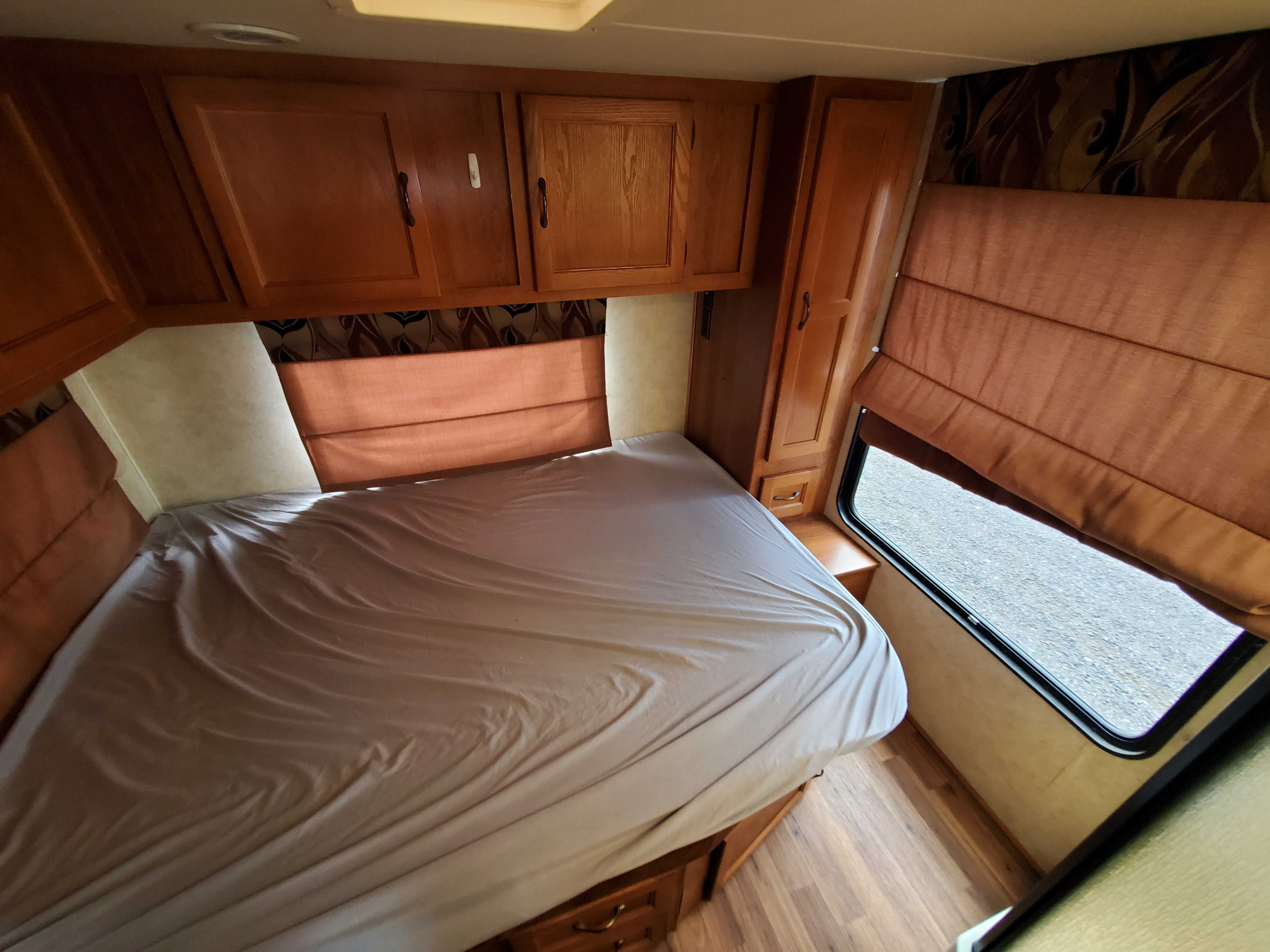 RV rental bedroom: large bed, overhead wooden cabinets, a wardrobe, and a window with a brown shade. Cozy and functional.. coachmen Freelander 2012