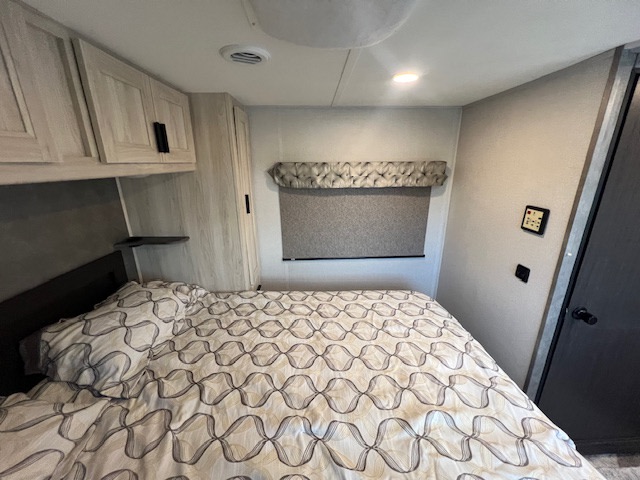 Cozy RV rental bedroom with patterned bed, light wood cabinets, and window. Ideal for comfortable travel trailer stays.. Forest River Sunseeker LE 2021