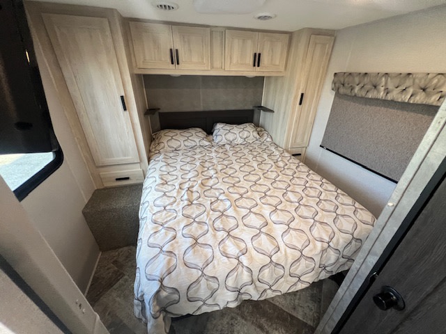 Cozy rv rental bedroom with patterned bed, light wood cabinets, storage, & window. Ideal for travel trailer stays.. Forest River Sunseeker LE 2021