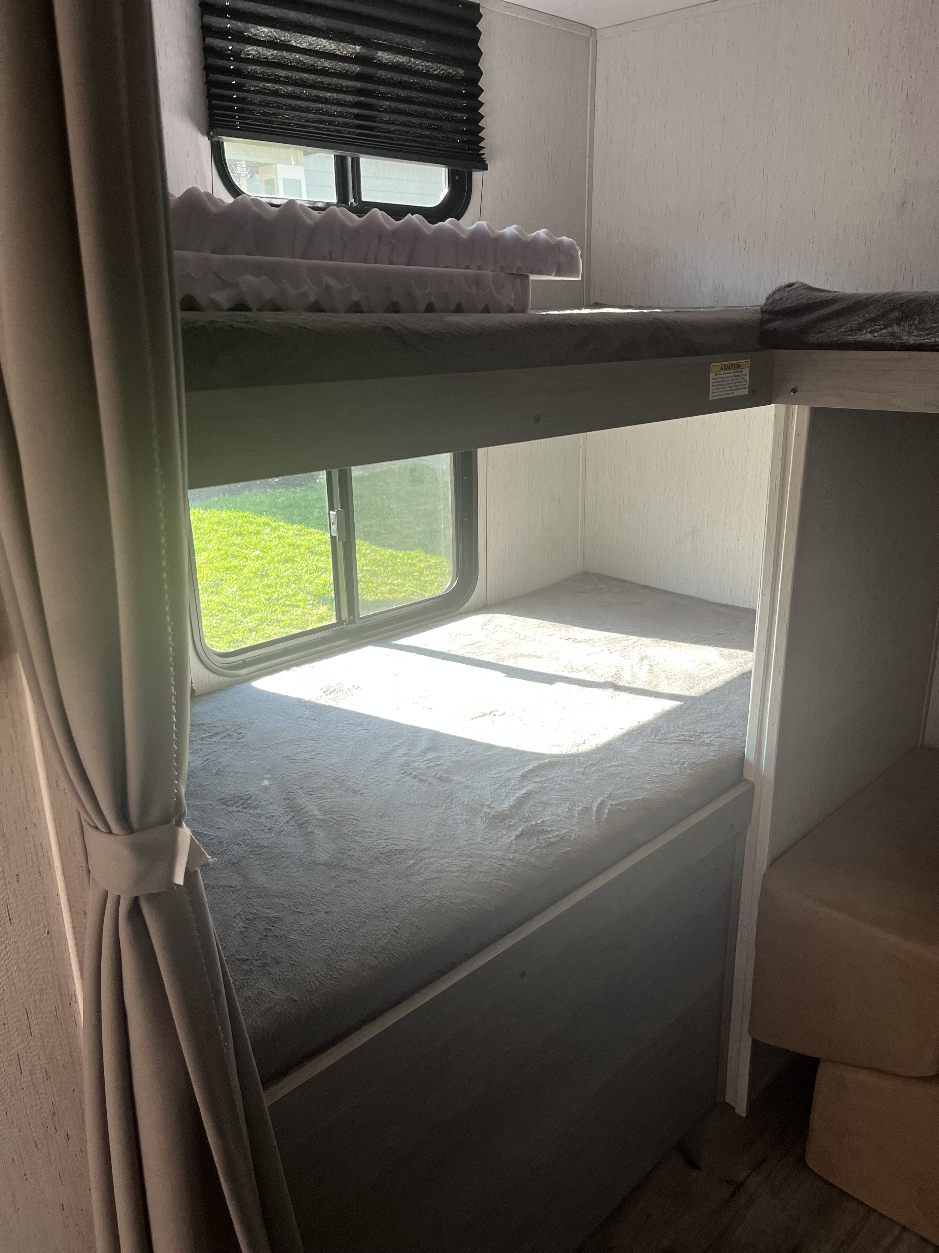 RV rental bunk beds: cozy interior with window, curtains, foam topper on top bunk, and gray blankets.. Dutchmen Coleman Lantern 2022
