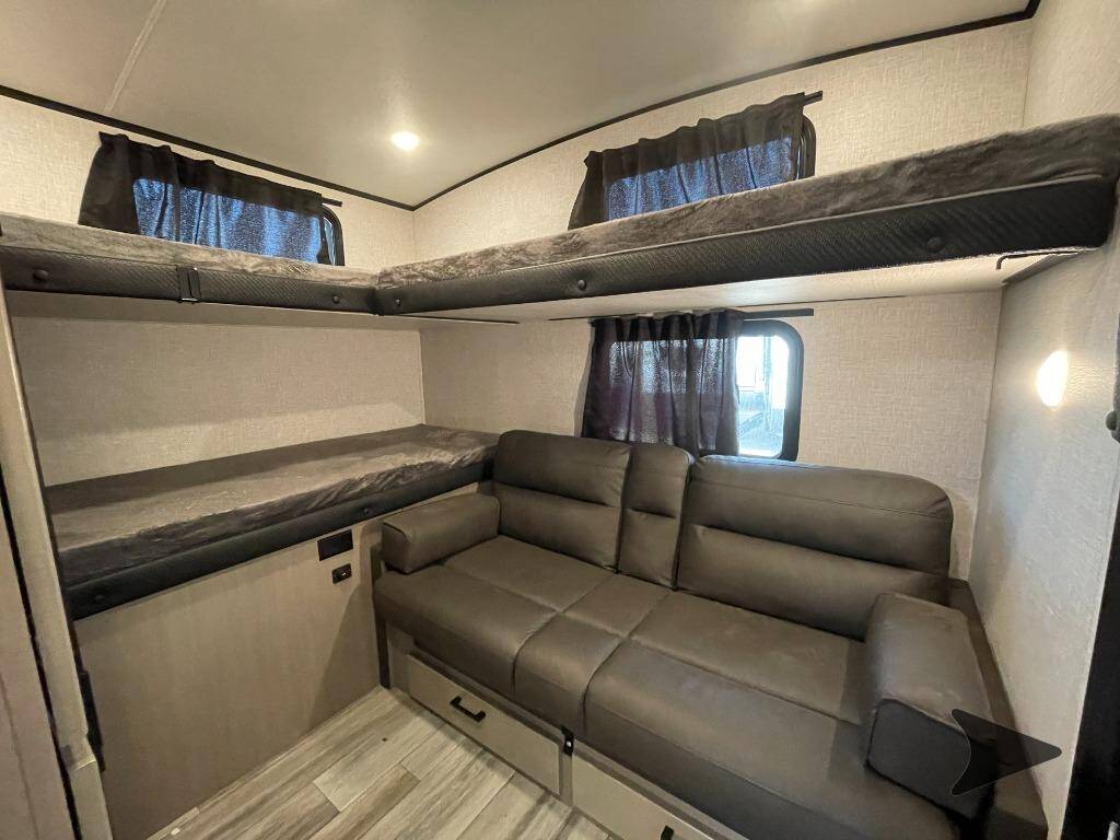 This RV rental interior features dark grey bunk beds on the left and upper right, alongside a sofa with storage drawers.. Jayco White Hawk 2024