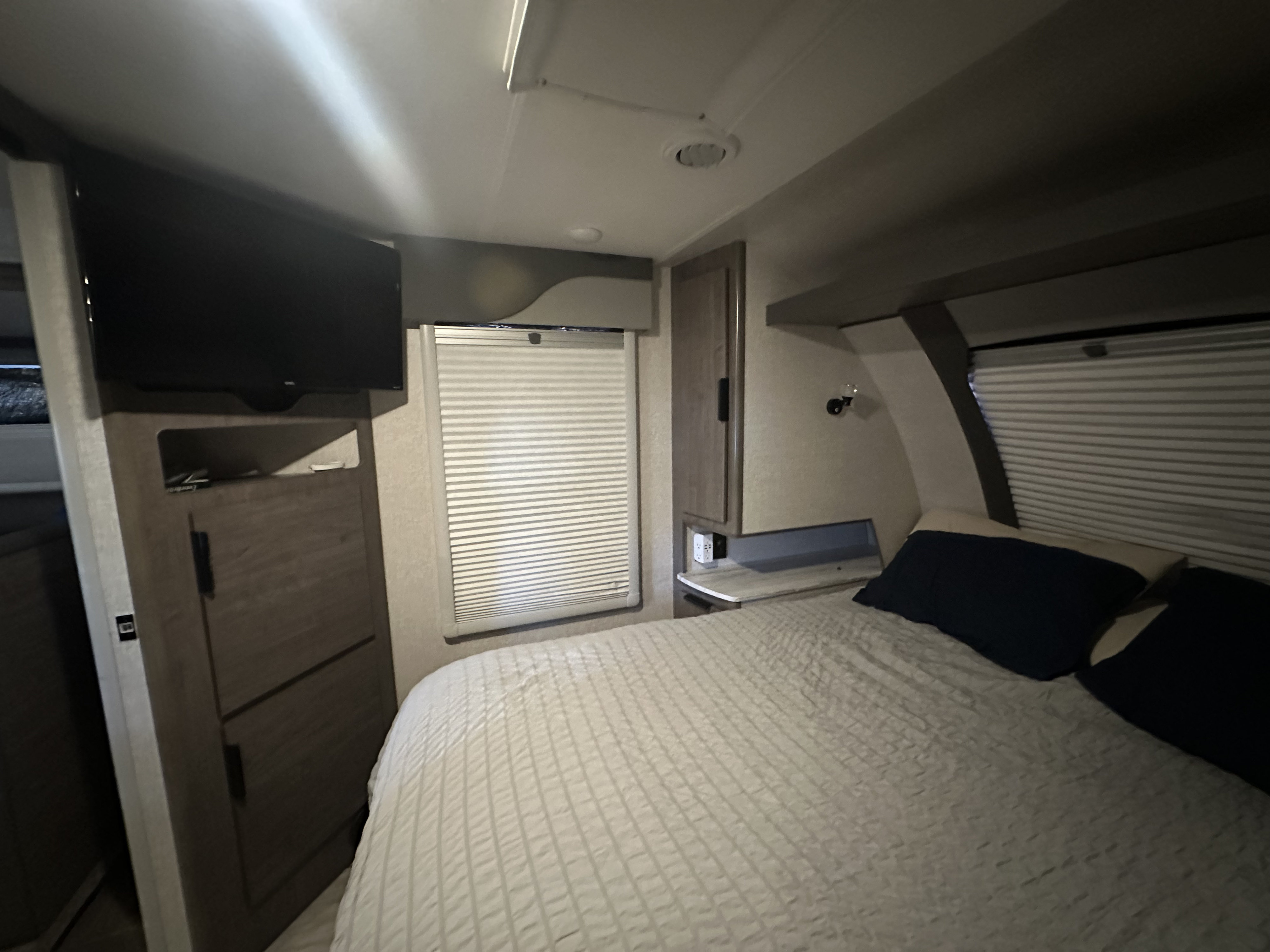 Experience comfort in this RV rental bedroom: features a cozy bed with dark pillows, TV, window blinds & ample storage.. Lance Manufacturing Lance Manufacturing Trailer 2022