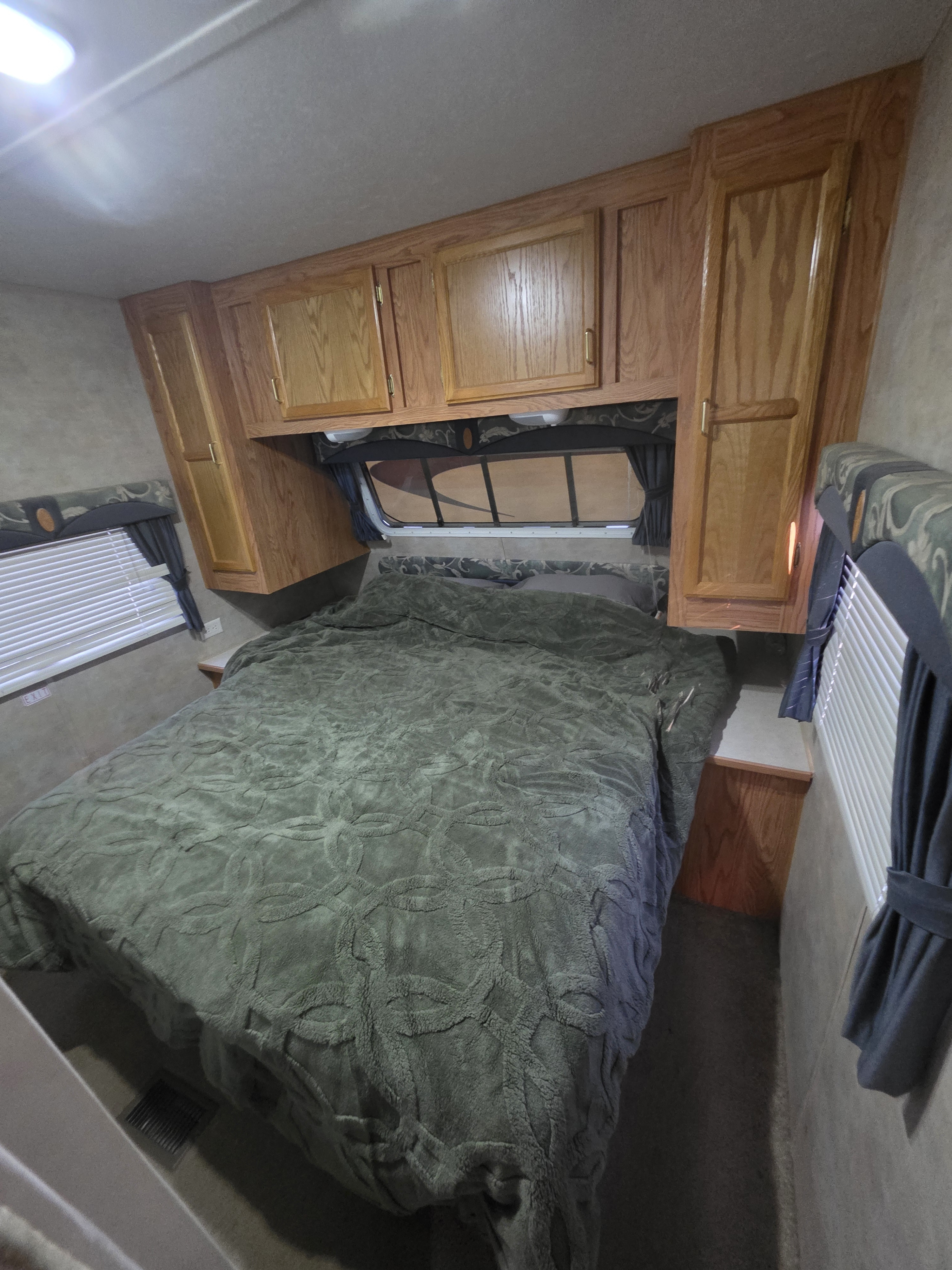 Compact RV rental bedroom with a comfy bed, wood cabinets, and windows, offering a cozy sleeping area for travel.. Jayco Jay Flight 2004