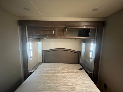 RV rental bedroom with a full-size bed, overhead storage cabinets, and side windows with blinds, ideal for road trips.. Jayco Greyhawk 2019