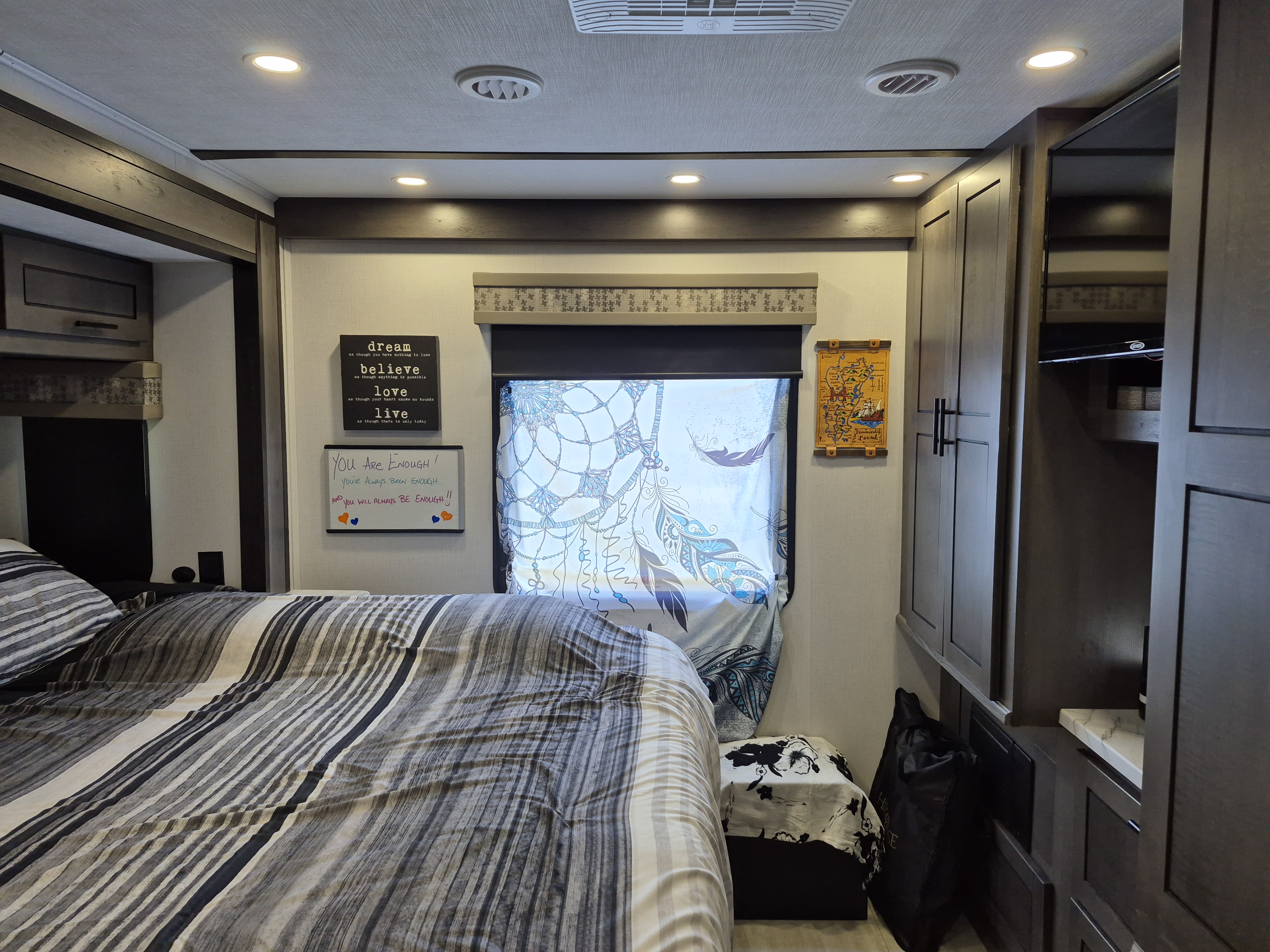 Comfortable RV rental bedroom featuring a striped bed, decorative window curtain, inspiring wall art, and practical storage.. Forest River FR3 2024