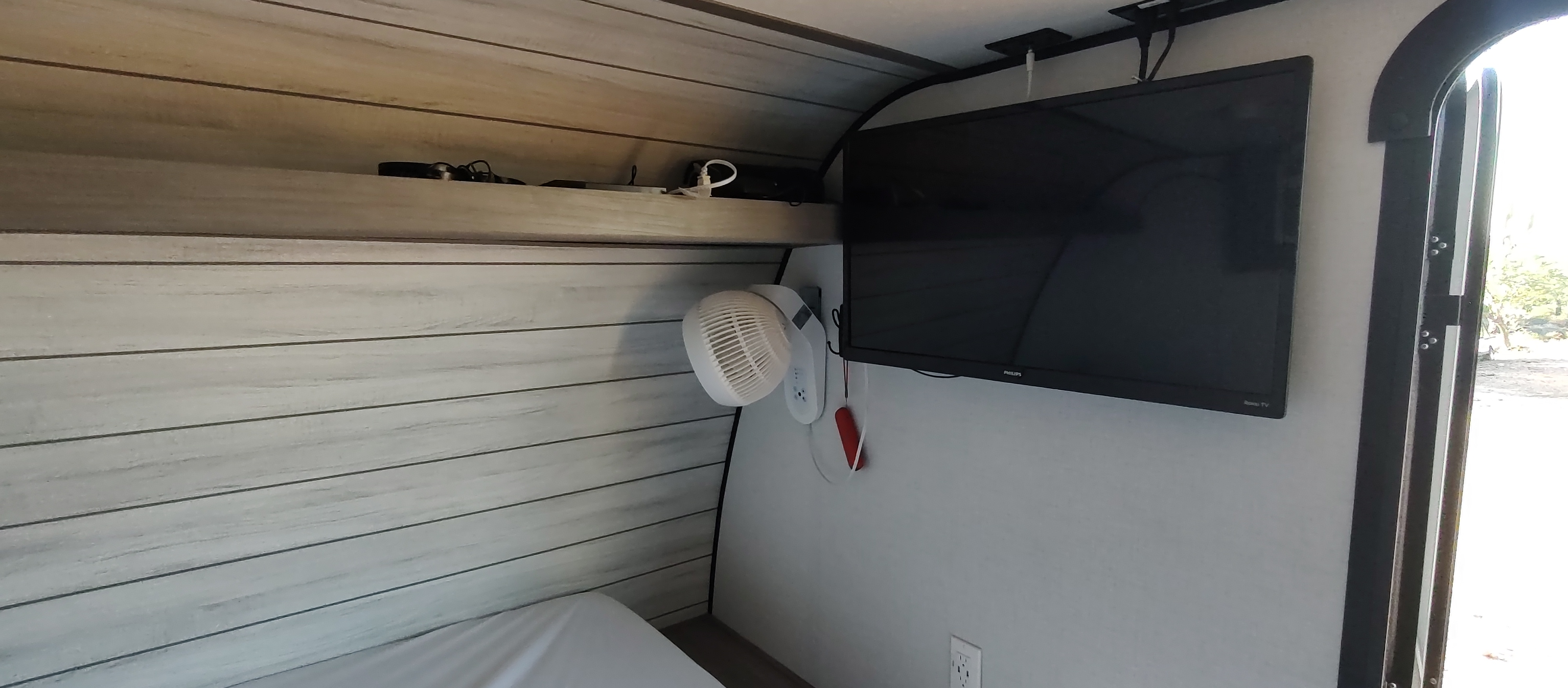 Compact RV rental interior featuring a bed, mounted TV, and fan. Perfect for mobile comfort on the road.. Dutchmen Lantern 17b 2024
