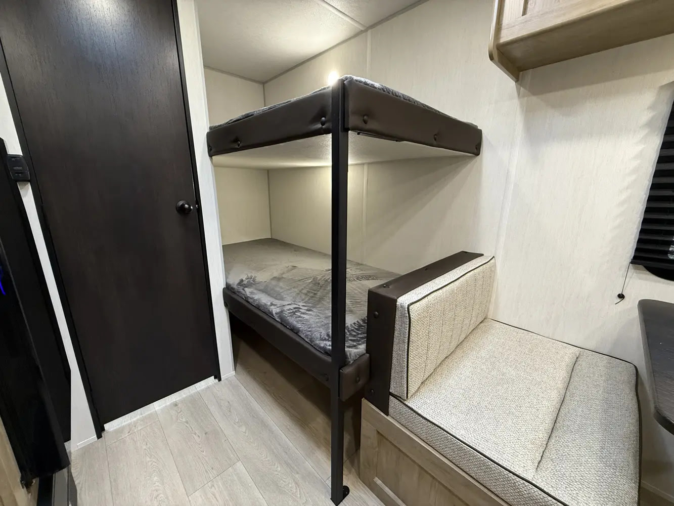 RV rental interior featuring two dark-framed bunk beds with gray bedding & a light beige upholstered seating area.. Forest River WOLFPUP 2026