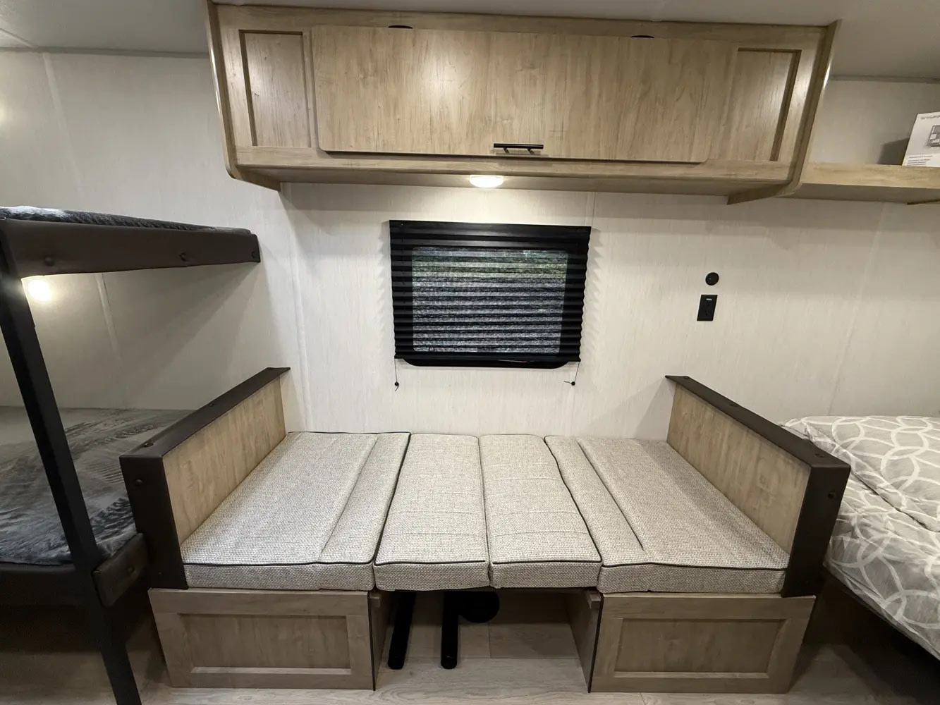 RV rental interior: Left, lower bunk bed. Center, a cushioned dinette below a window and wood overhead cabinets. Right, a bed.. Forest River WOLFPUP 2026