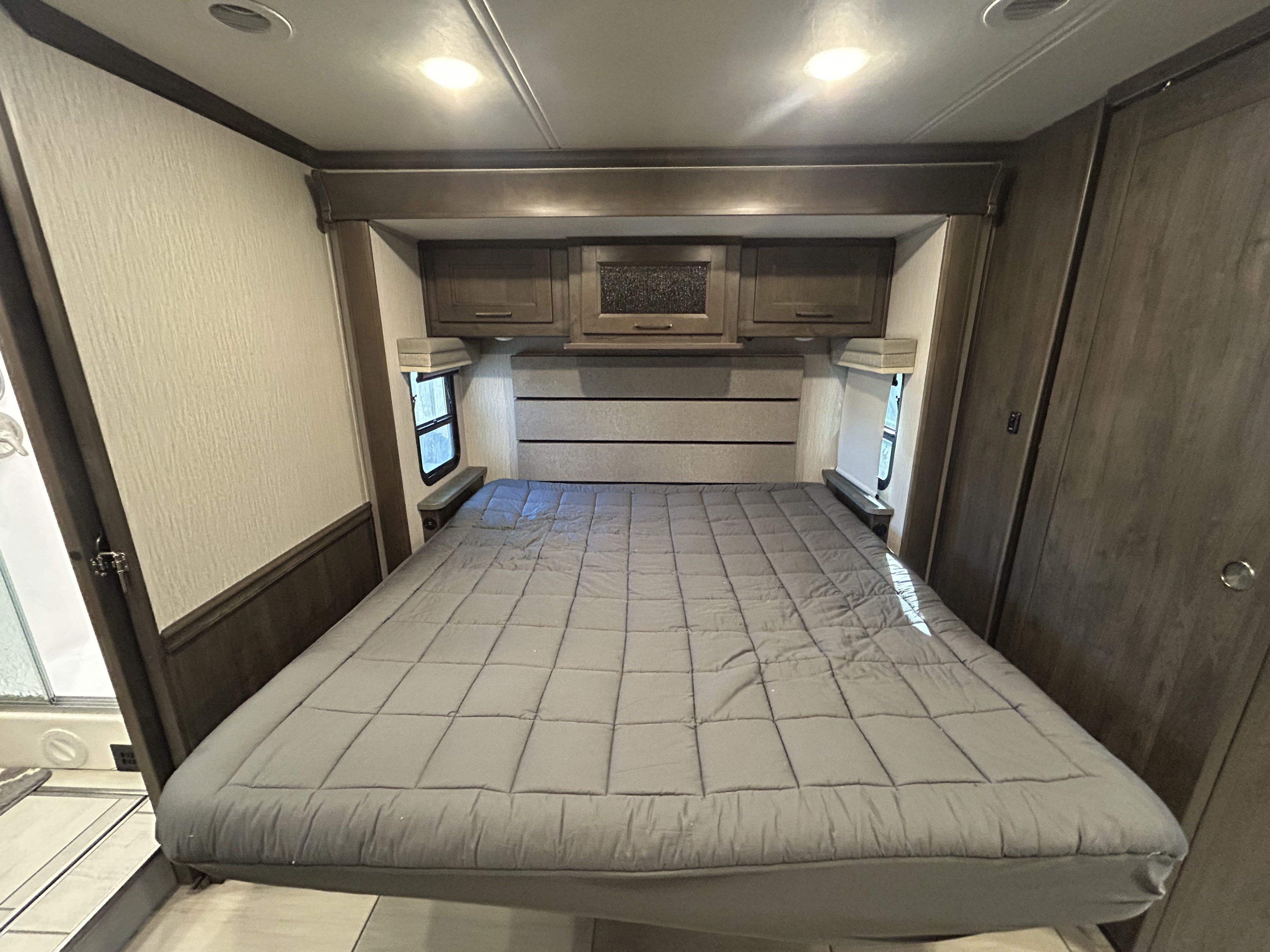 Modern RV rental bedroom featuring a large bed, overhead cabinets, and windows for natural light, perfect for comfortable travel.. Forest River Coachmen Sportscoach RD 2021