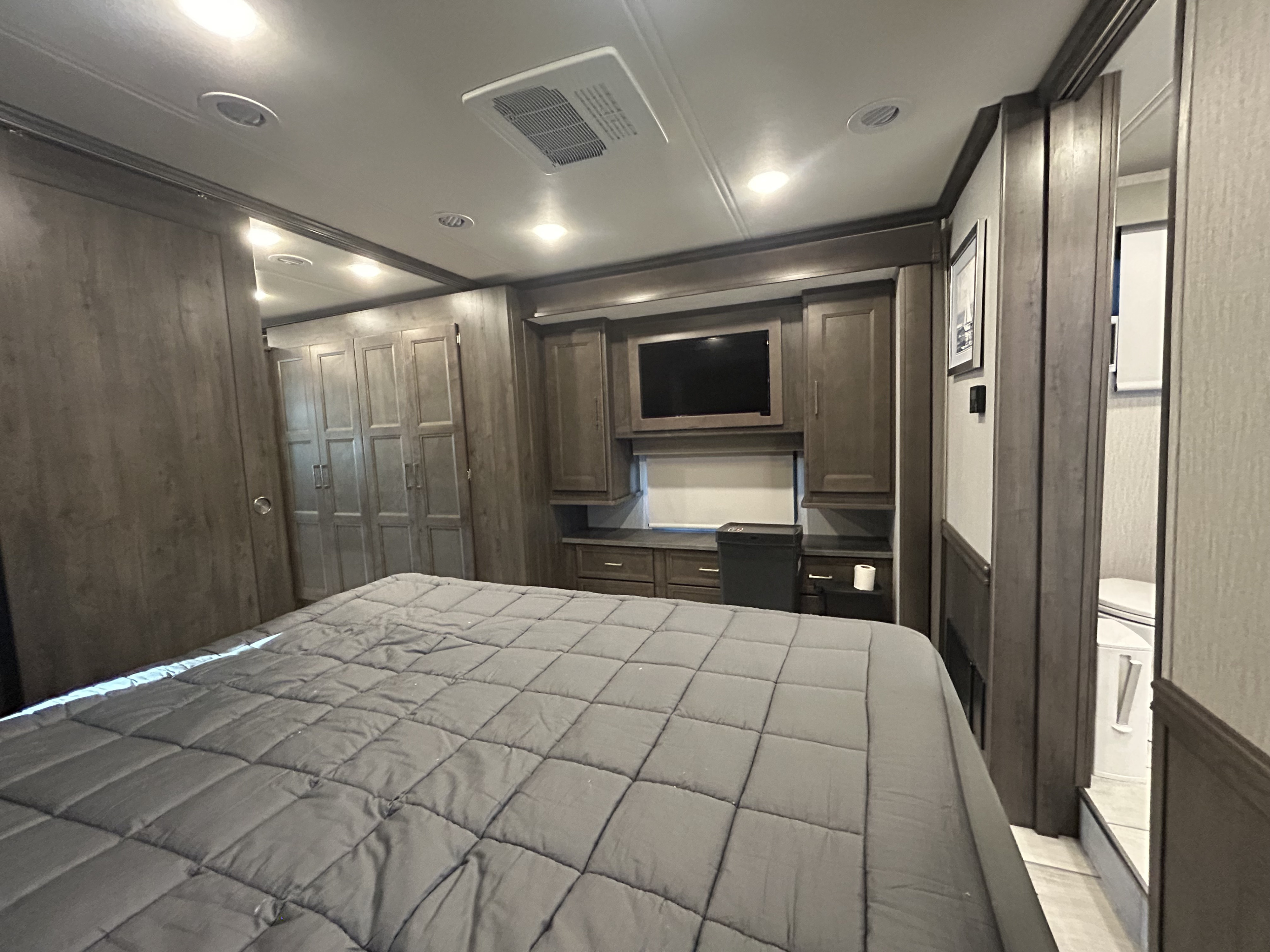 Spacious RV rental bedroom featuring a comfortable bed, built-in storage, TV, and adjacent bathroom.. Forest River Coachmen Sportscoach RD 2021