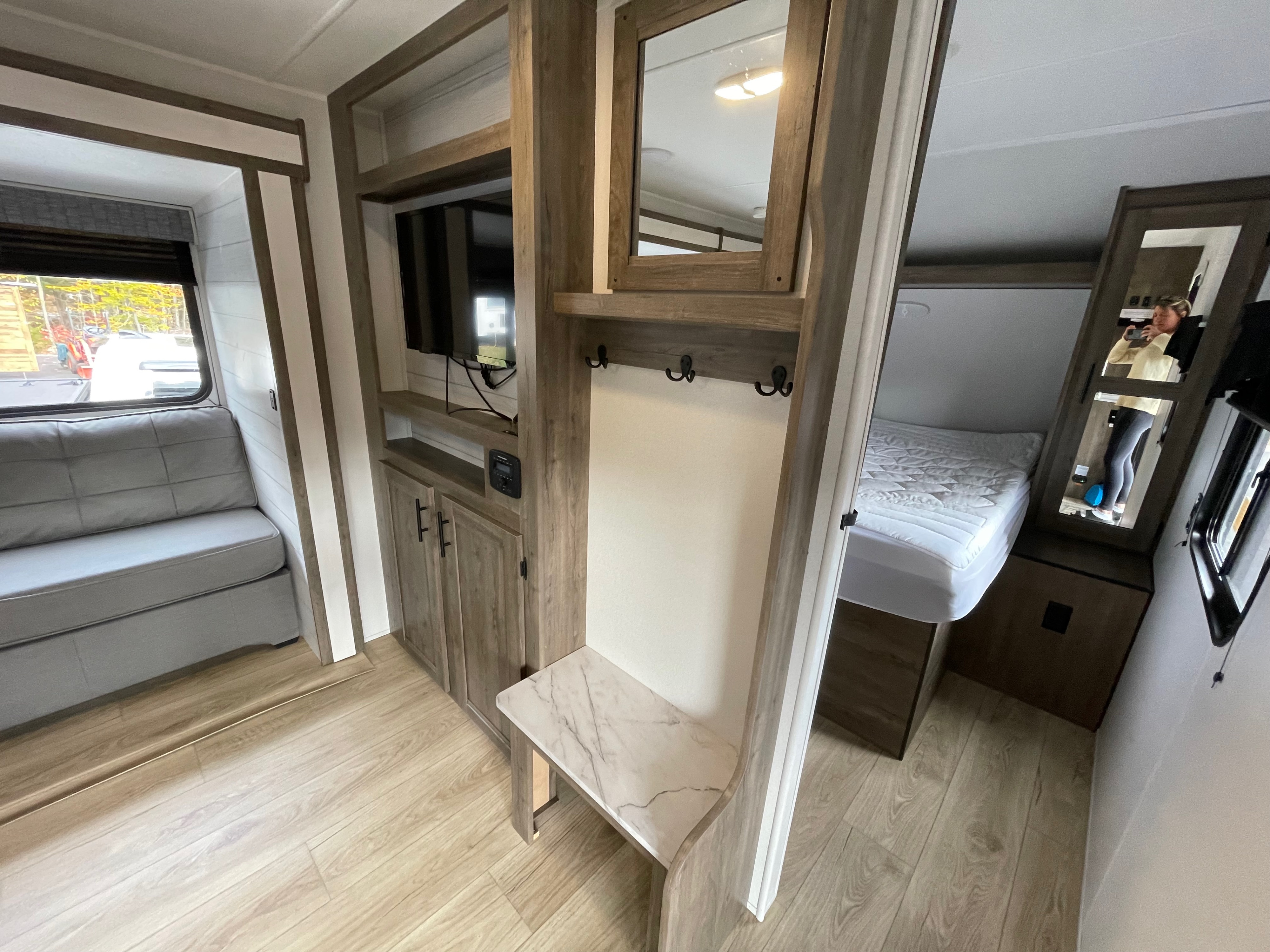 Modern rv rental interior: bright space with gray sofa, TV, cabinets, coat hooks, and comfortable bed beyond.. Heartland Pioneer 2024