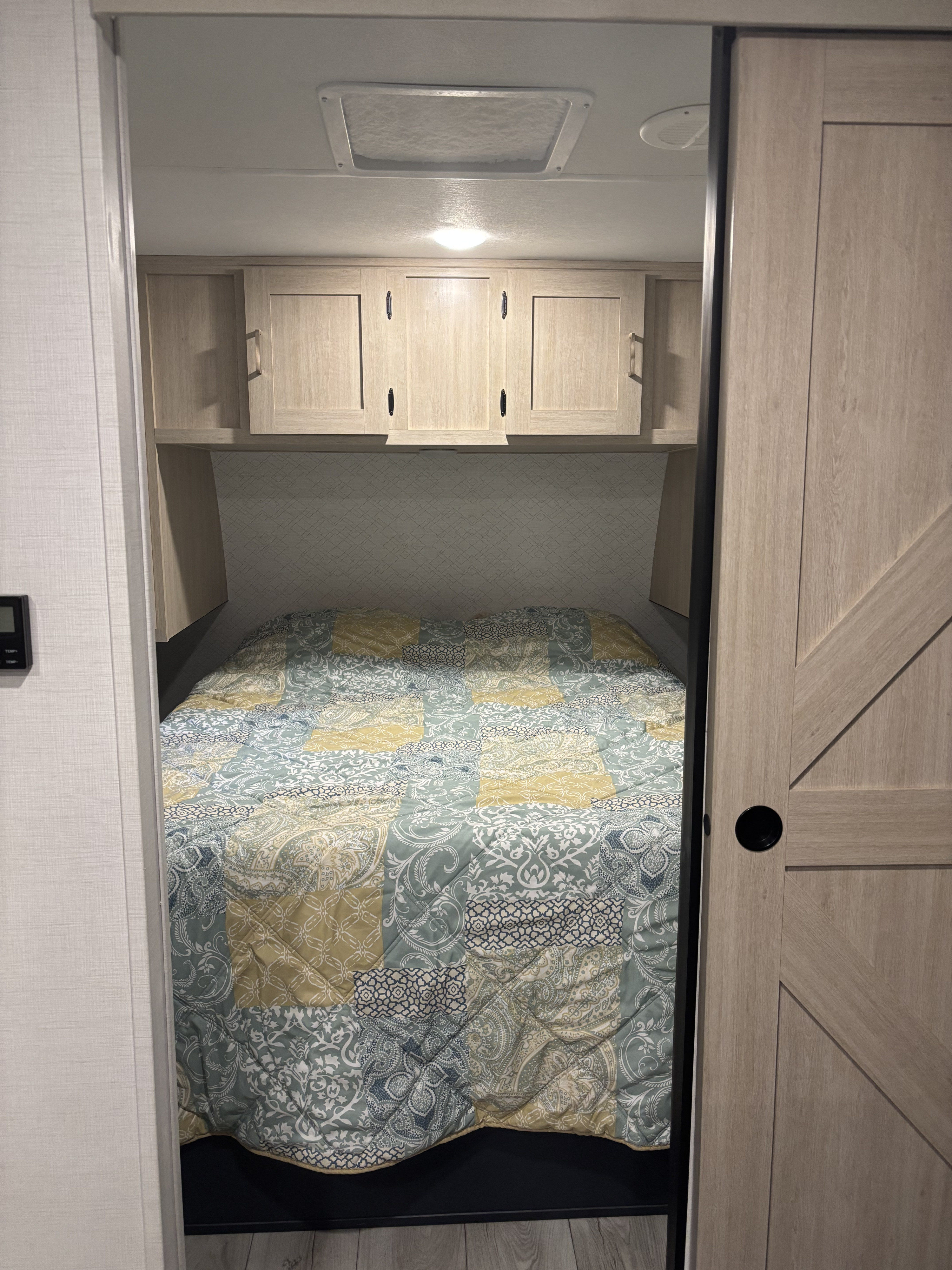 This RV rental bedroom features a comfy bed with a patchwork quilt, overhead cabinets, a ceiling vent, and a sliding door.. Forest River, Inc. Primetime Avenger 2025