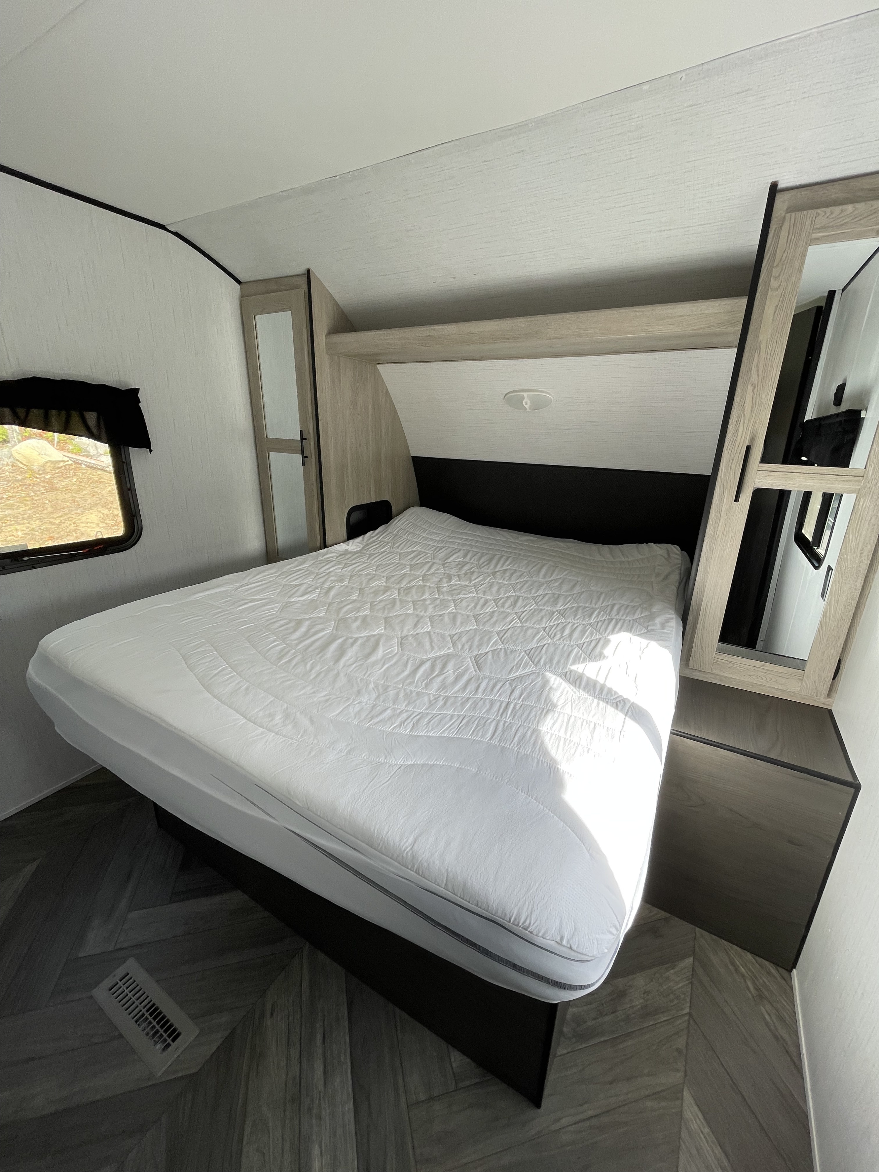 Clean RV rental bedroom featuring a bed with white bedding, built-in cabinets, and modern wood-look floor. Ready for your trip.. Heartland Prowler 2022
