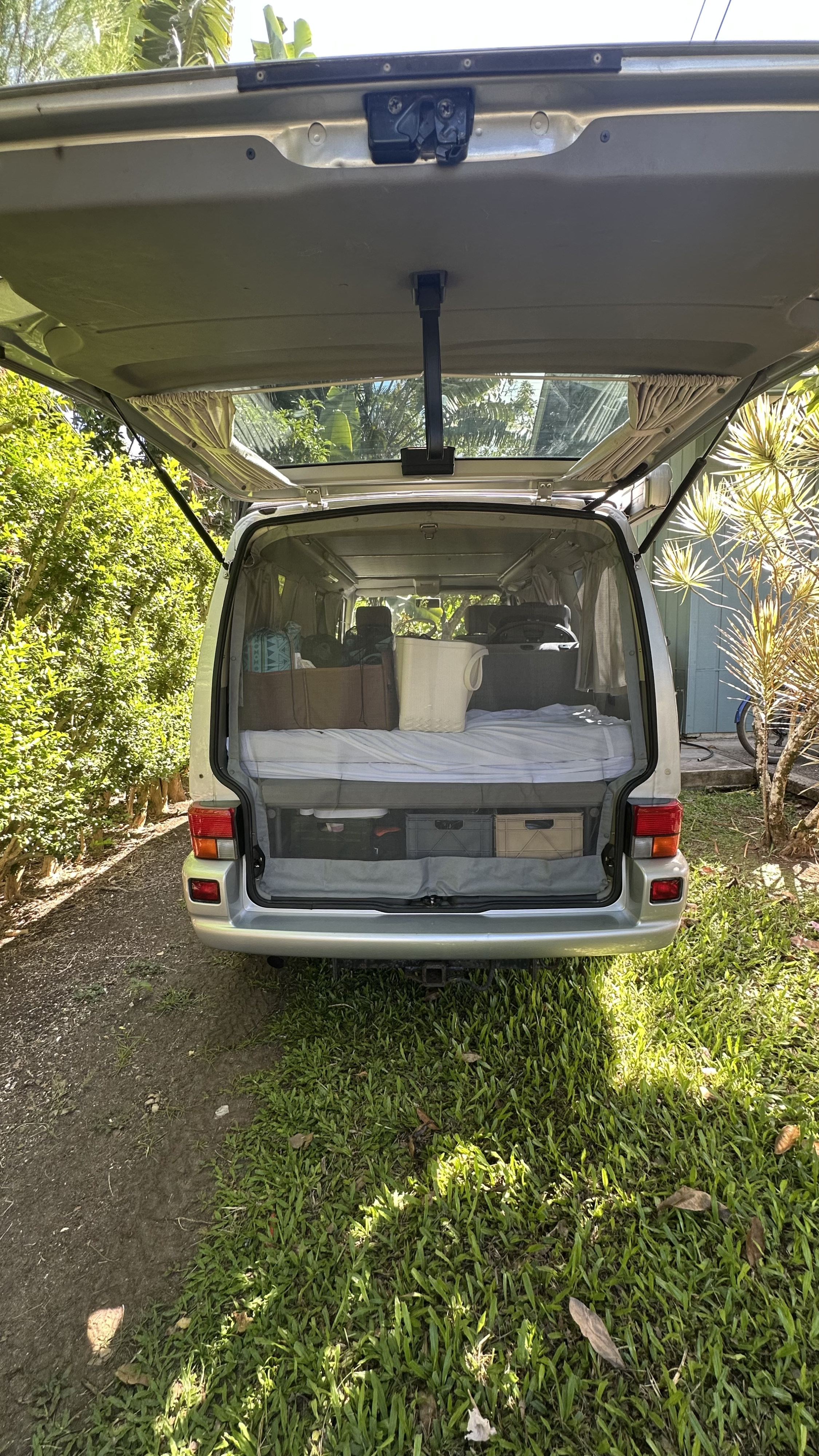Tailgate open on a silver camper van (RV rental), revealing a bed, storage, and mesh screen for outdoor adventures.. Volkswagen Westfalia 2002