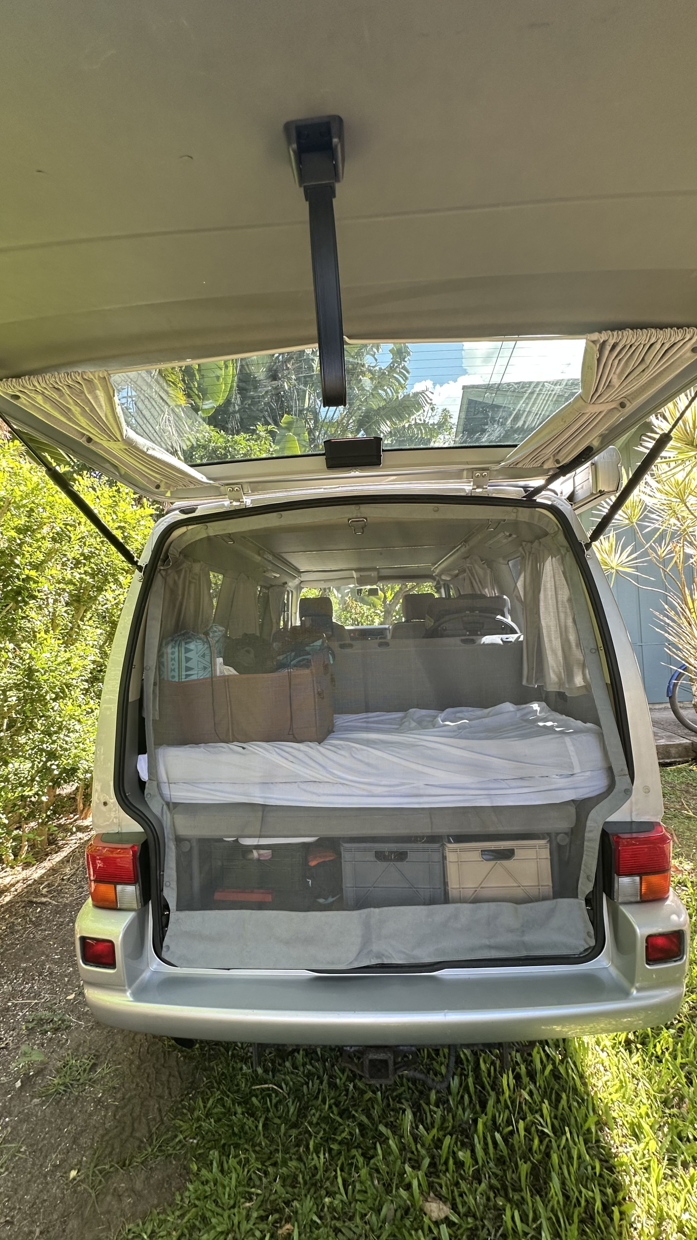 RV rental camper van interior with open rear hatch, showing a bed, storage crates, and protective insect mesh.. Volkswagen Westfalia 2002