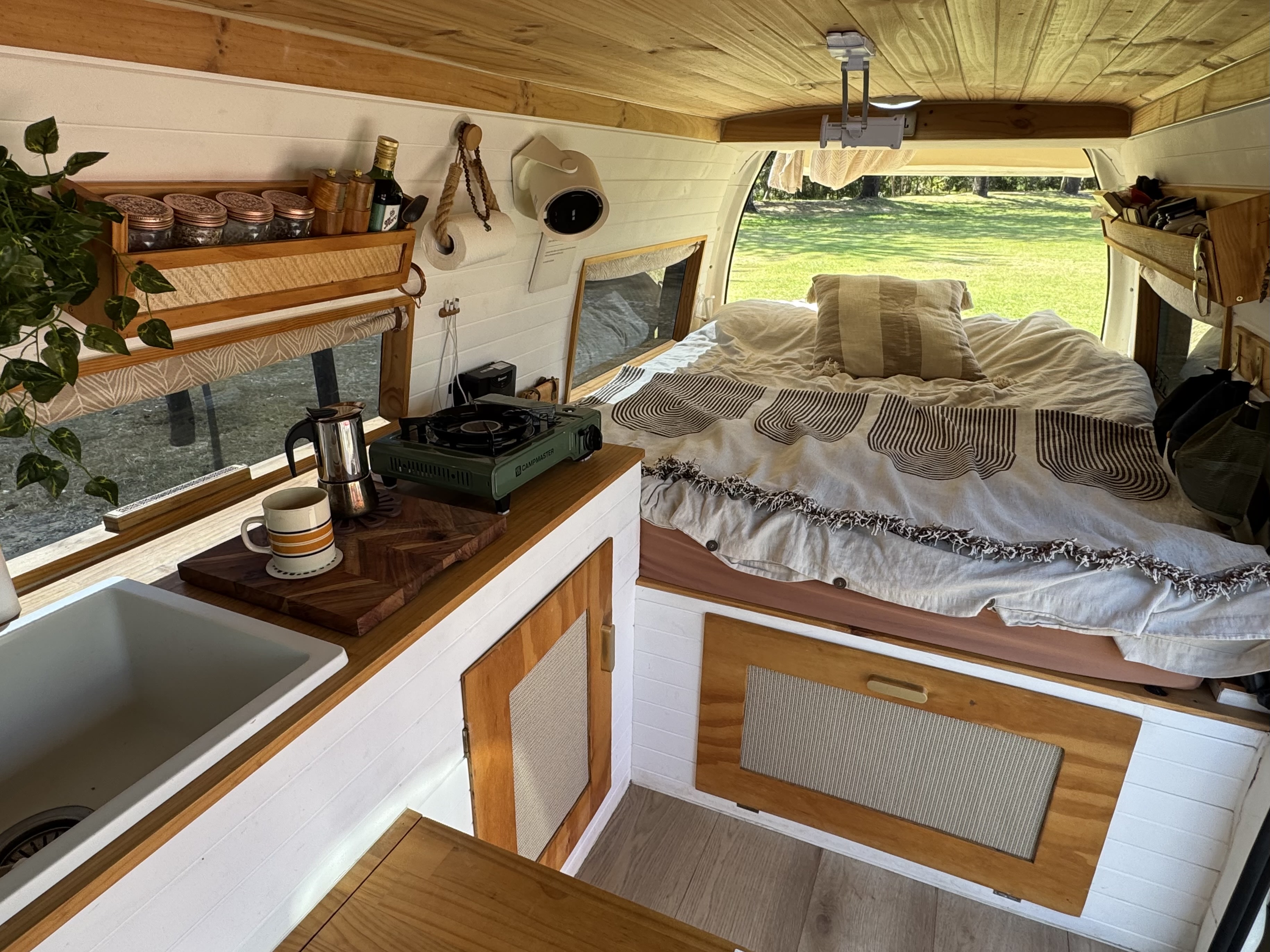 Explore this stylish RV rental's interior: a compact kitchen, comfy bed, and ceiling projector, with scenic outdoor views.. Toyota Hiace Campervan 2006