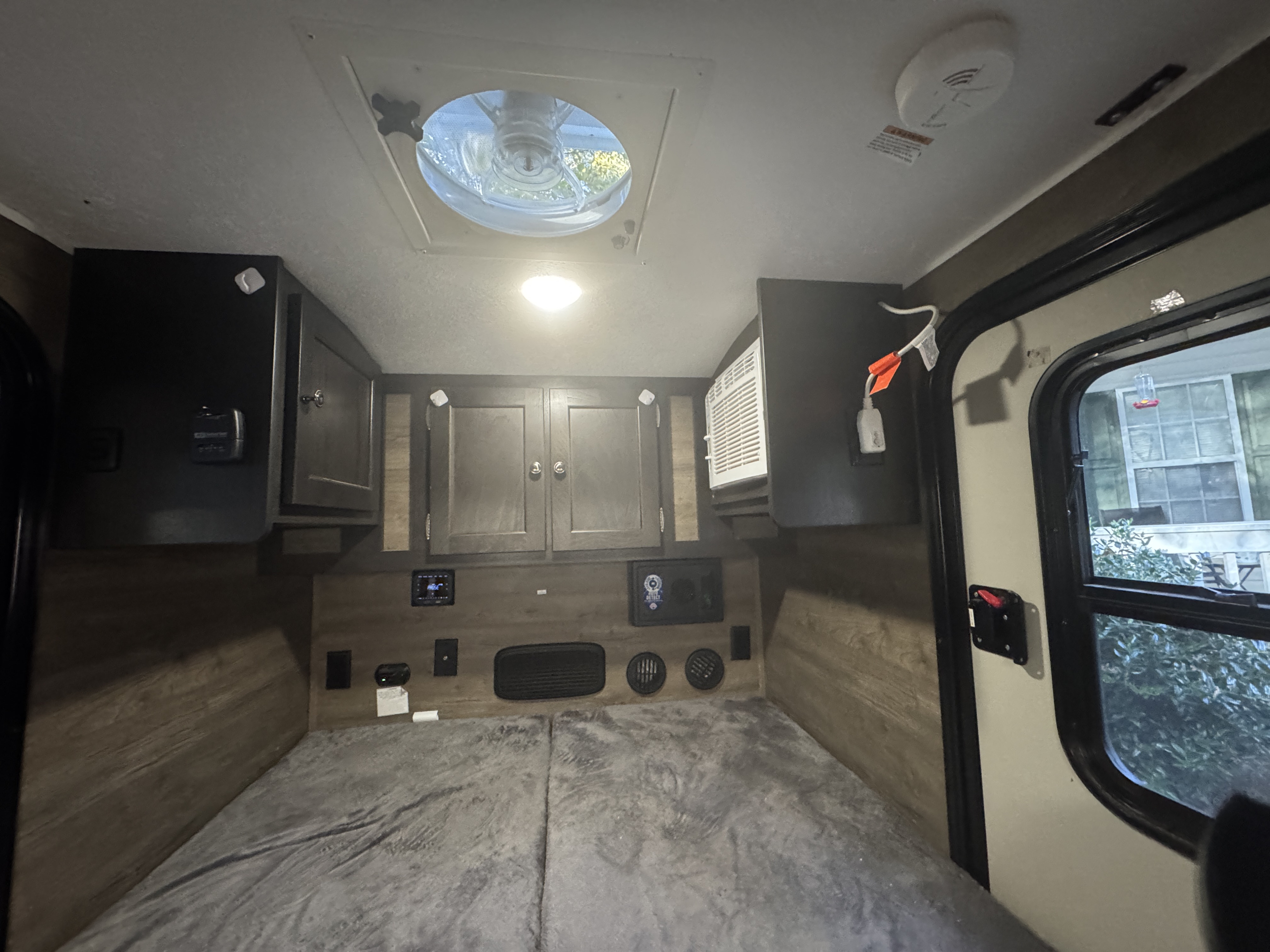 Comfortable RV rental bedroom with gray bedding, overhead storage, ceiling fan, AC, and control panel for an enjoyable camper stay.. Braxton Creek Bushwhacker 2022