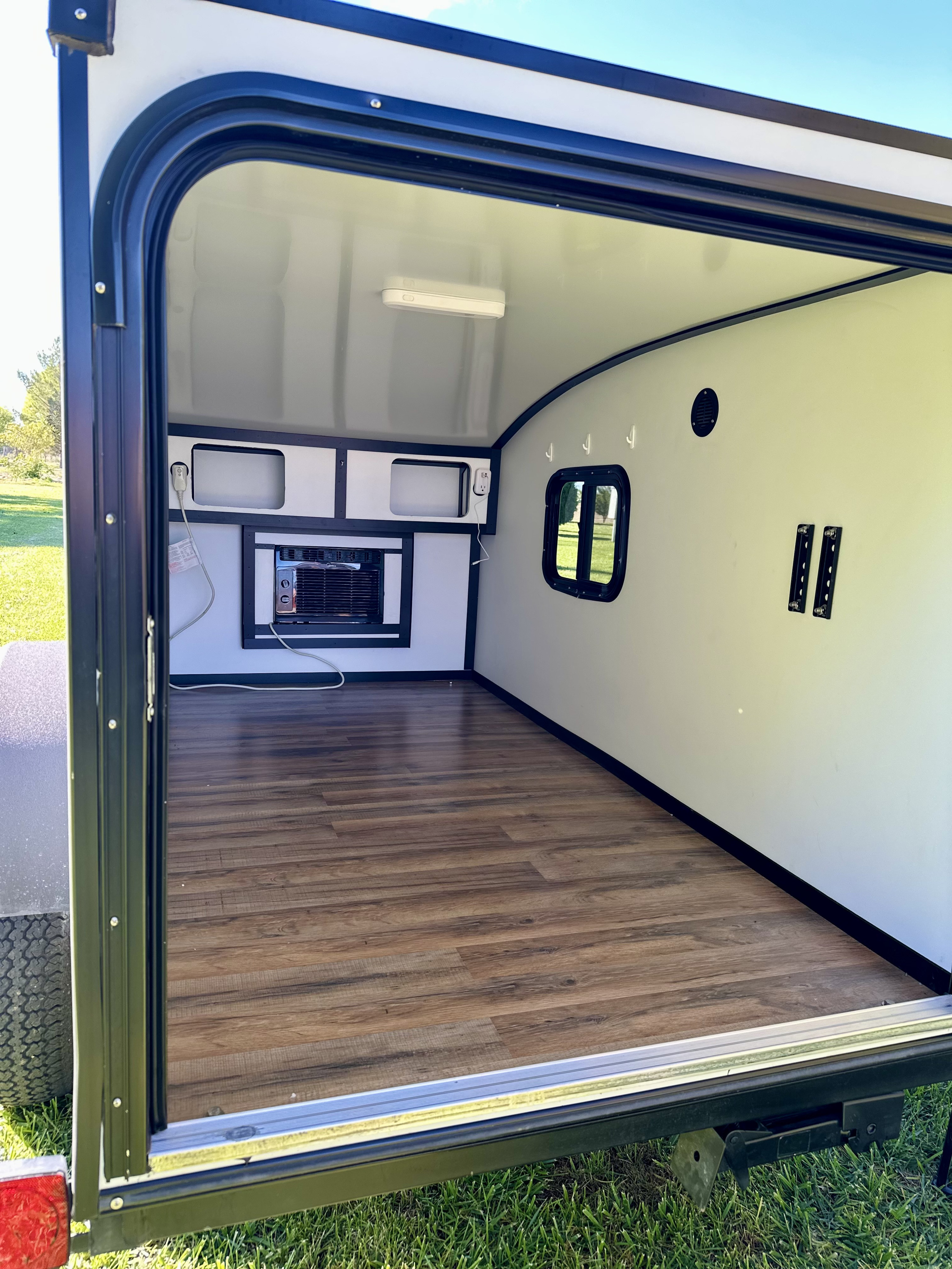 Inside a clean RV rental: wood-look floor, white walls, AC, window, and wall mounts for comfort on the go.. Tiny Camper Co Squaredrop 2024