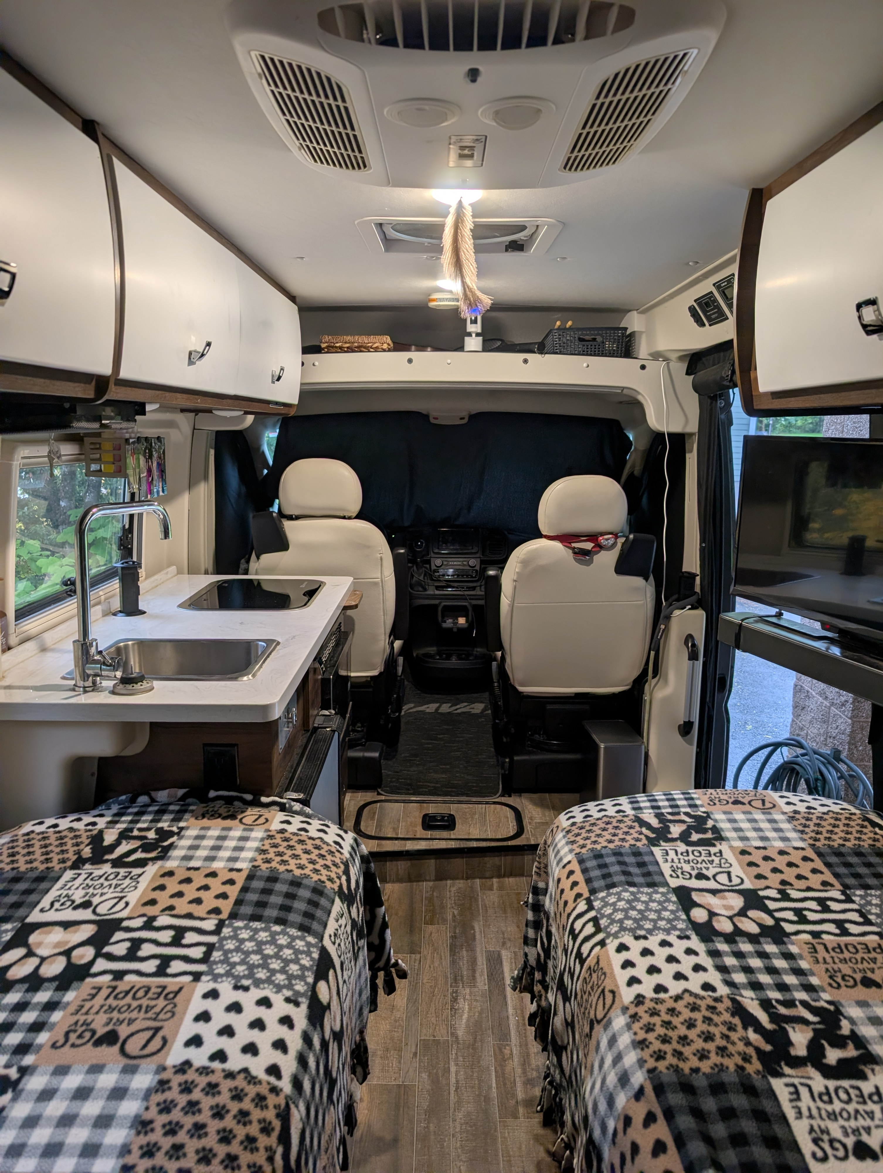 Inside this RV rental, find a functional kitchenette, twin beds with dog-themed blankets, and the front cab area.. Winnebago Travato 2022