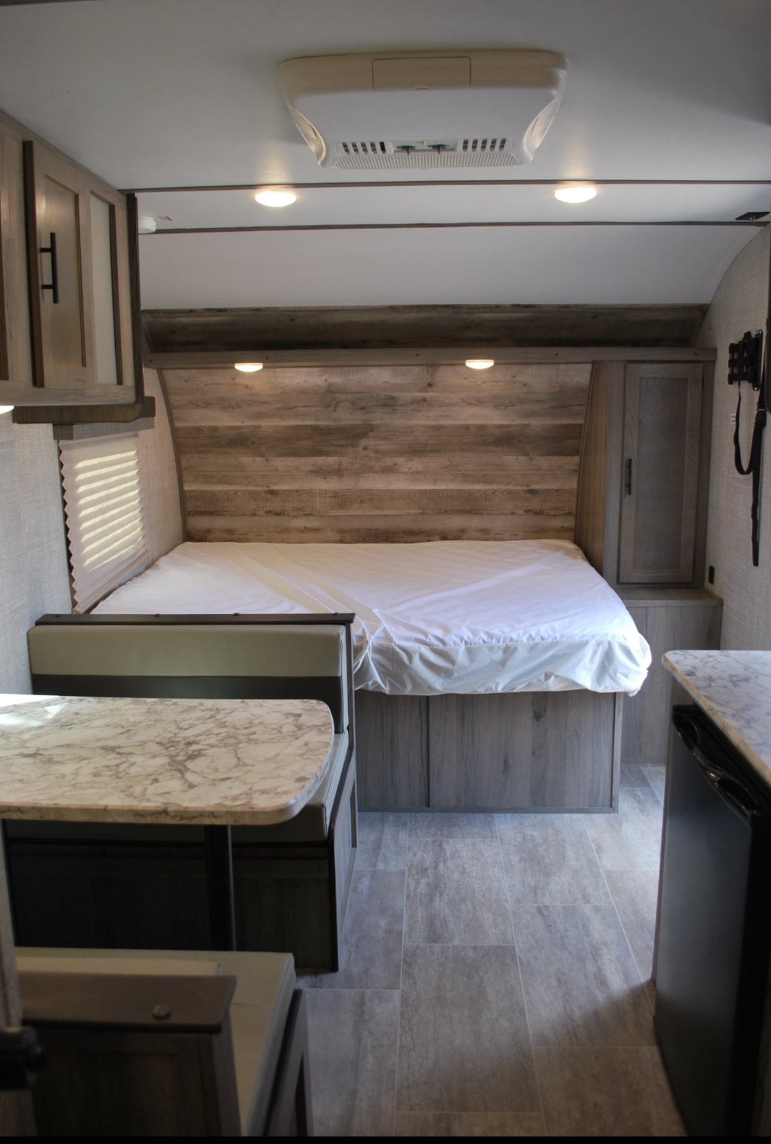 Cozy RV rental interior featuring a bed, dinette, and modern wood finishes. Perfect for travel trailer adventures!. Gulf Stream Ameri-Lite Super Lite 2020