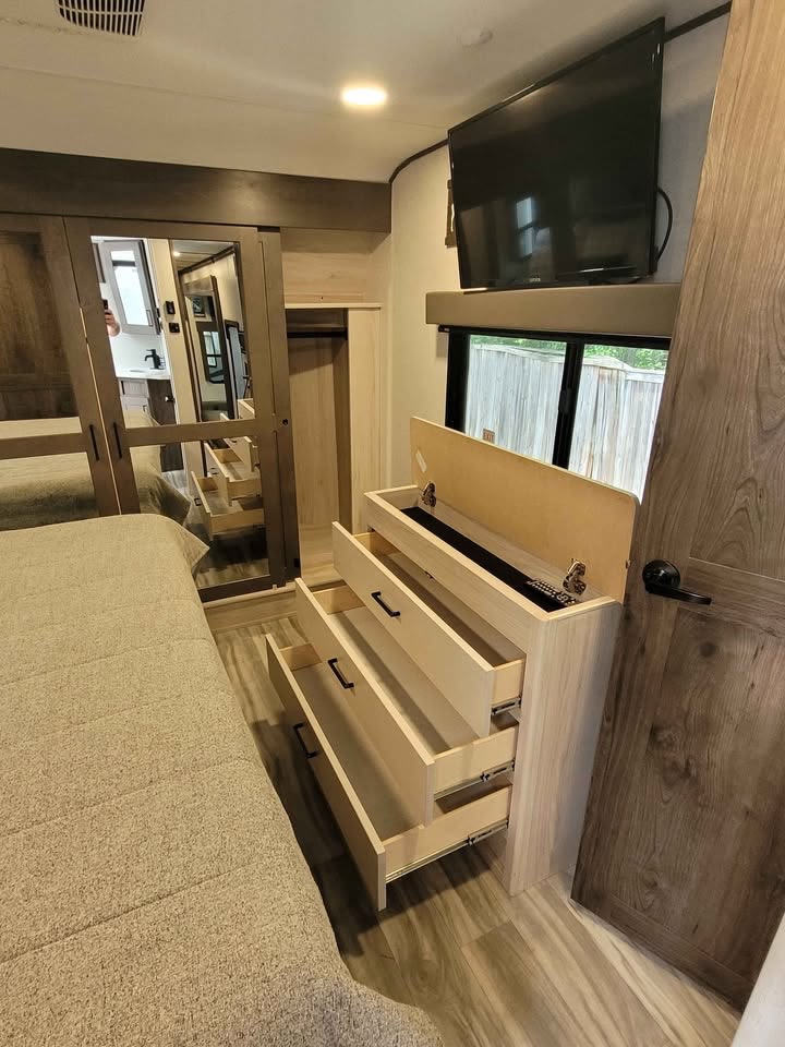 This RV rental bedroom features a comfy bed, dresser with open drawers & top storage for remotes, mounted TV, and mirrored closet.. Alliance Valor 2022