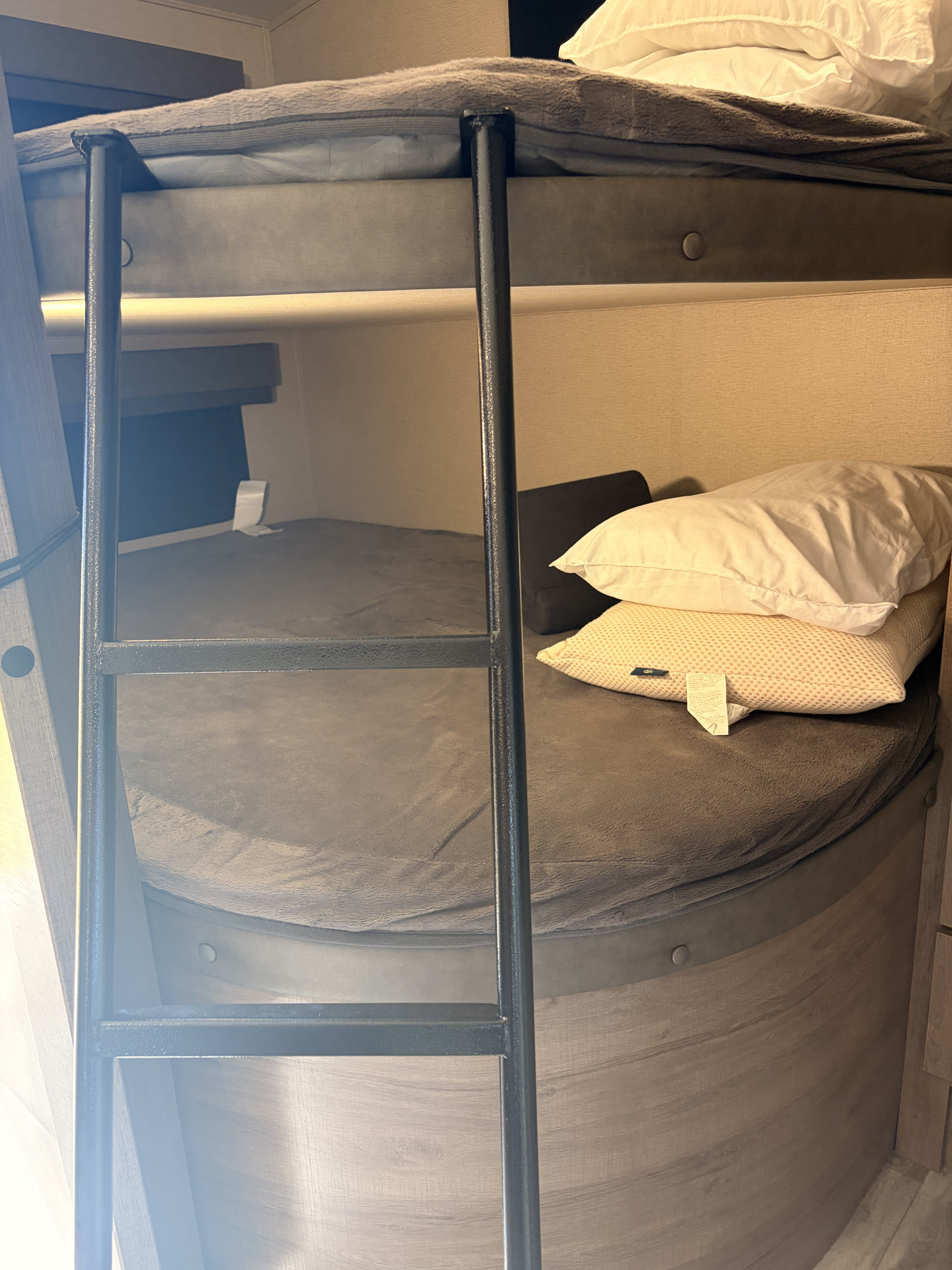 Cozy RV rental interior featuring modern bunk beds with a ladder for access, dressed in neutral bedding.. Grand Design Imagine 2023