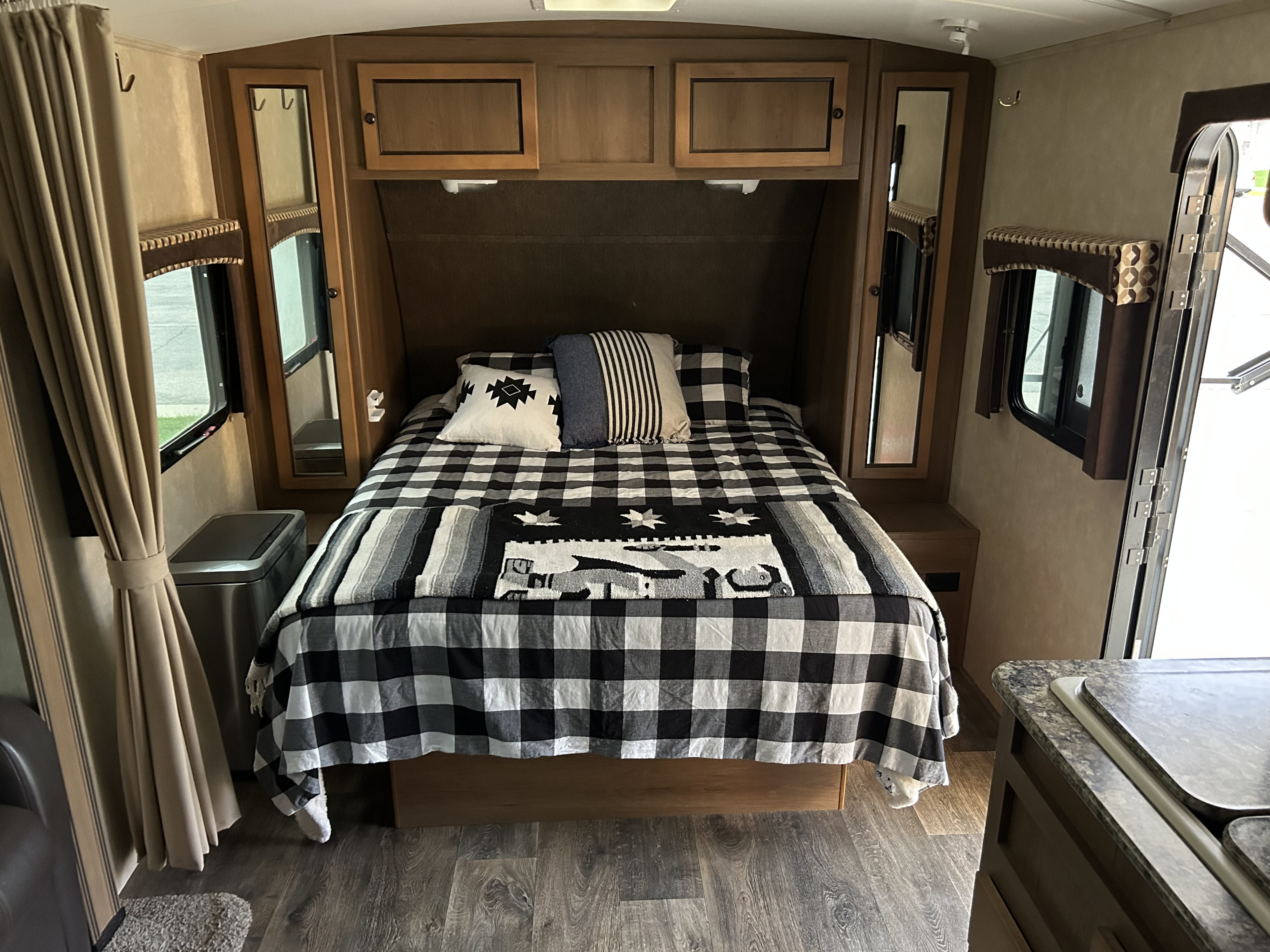 Cozy RV rental bedroom showcasing a bed with black & white checkered bedding, wood cabinets, and large windows with curtains.. Cruiser RV Shadow Cruiser 2015
