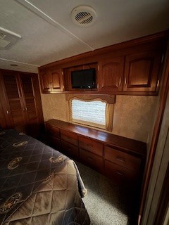 Cozy RV rental bedroom with built-in cabinets, drawers, TV, window, and a comfortable bed.. Keystone RV Alpine 2011